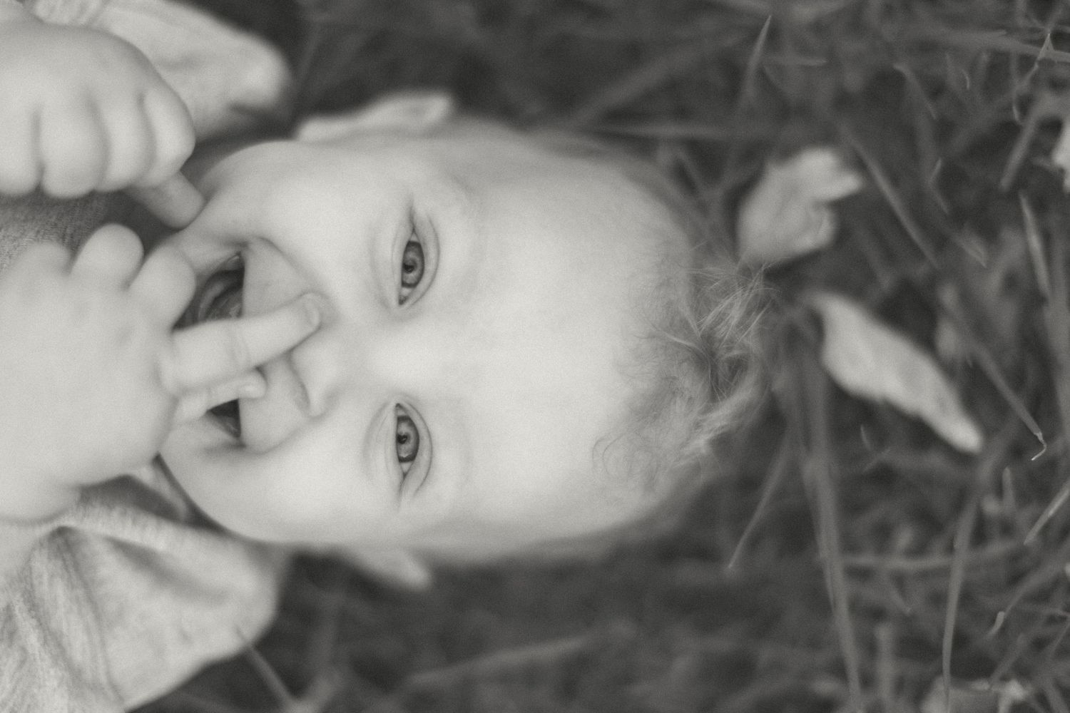 Baby boy laying in the grass while laughing up at the camera.