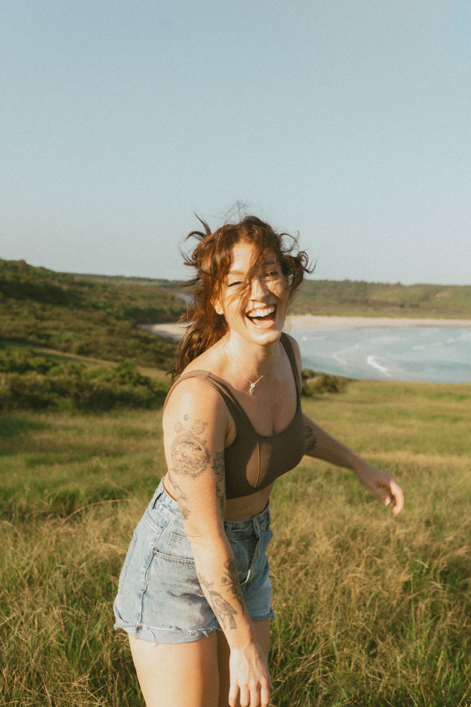 Woman standing field with messy hair laughing and looking at the camera.
