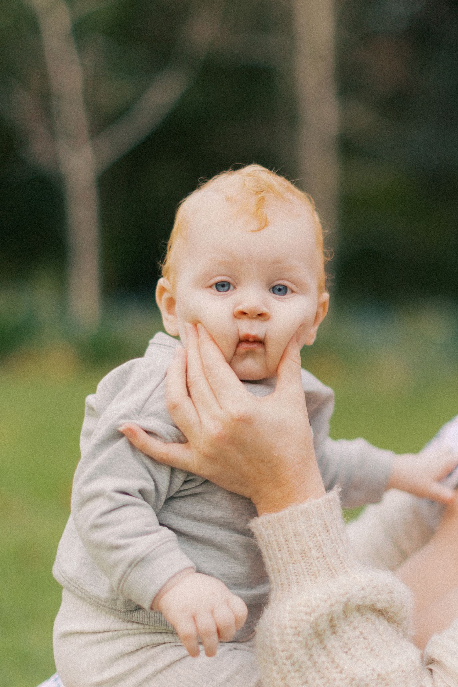Baby boy looking at camera while his mother squishes his chubby cheeks.