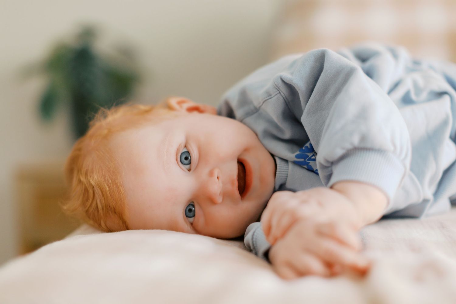 Baby boy with bright ginger hair and blue eyes laying on his side and smiling at the camera.
