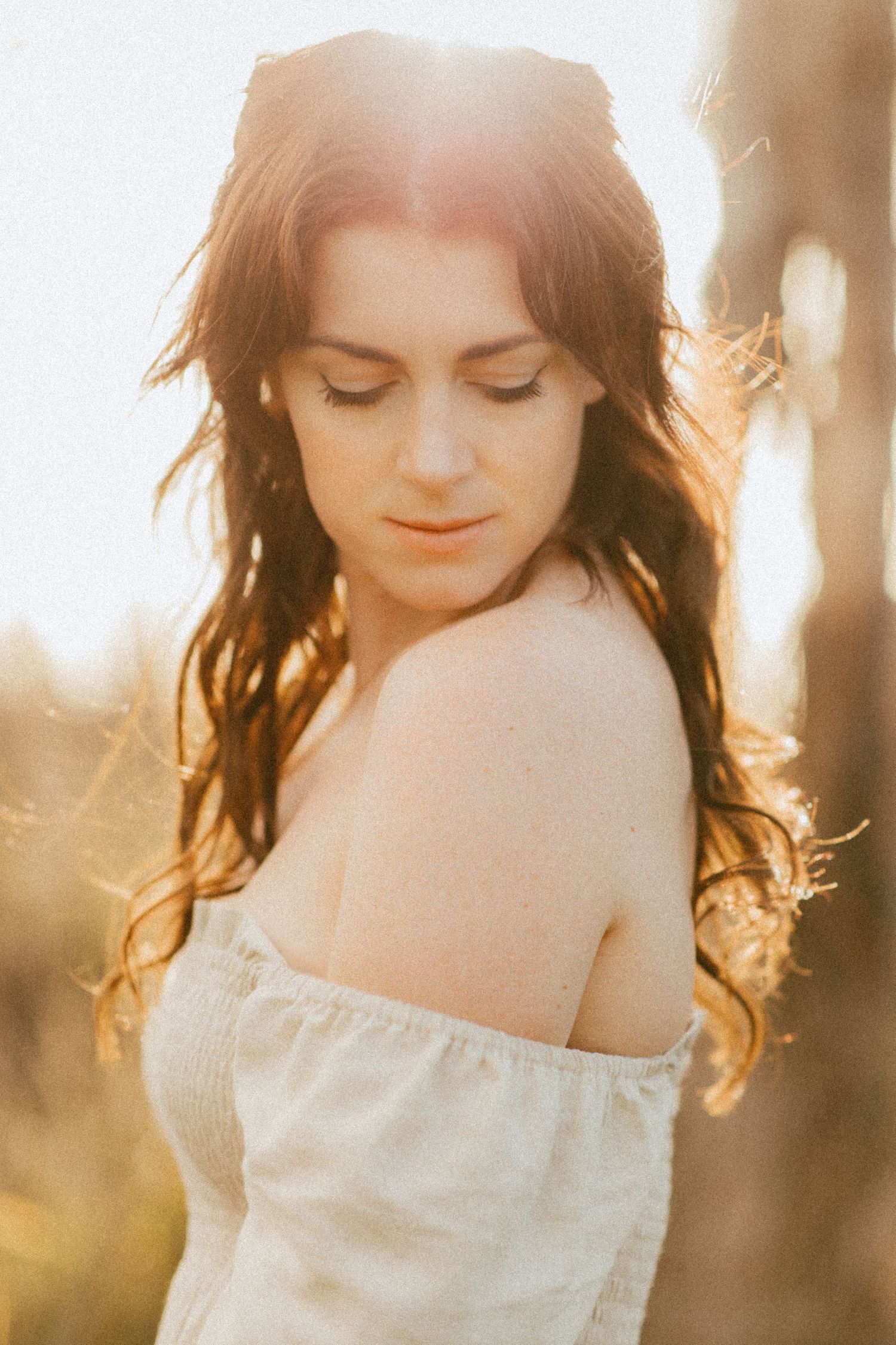 Woman looking down over her shoulder while being backlit by the golden hour sunshine.