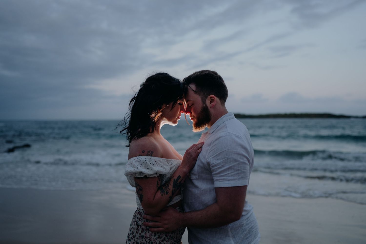 Couple leaning foreheads together at dusk at the beach in Port Kembla.