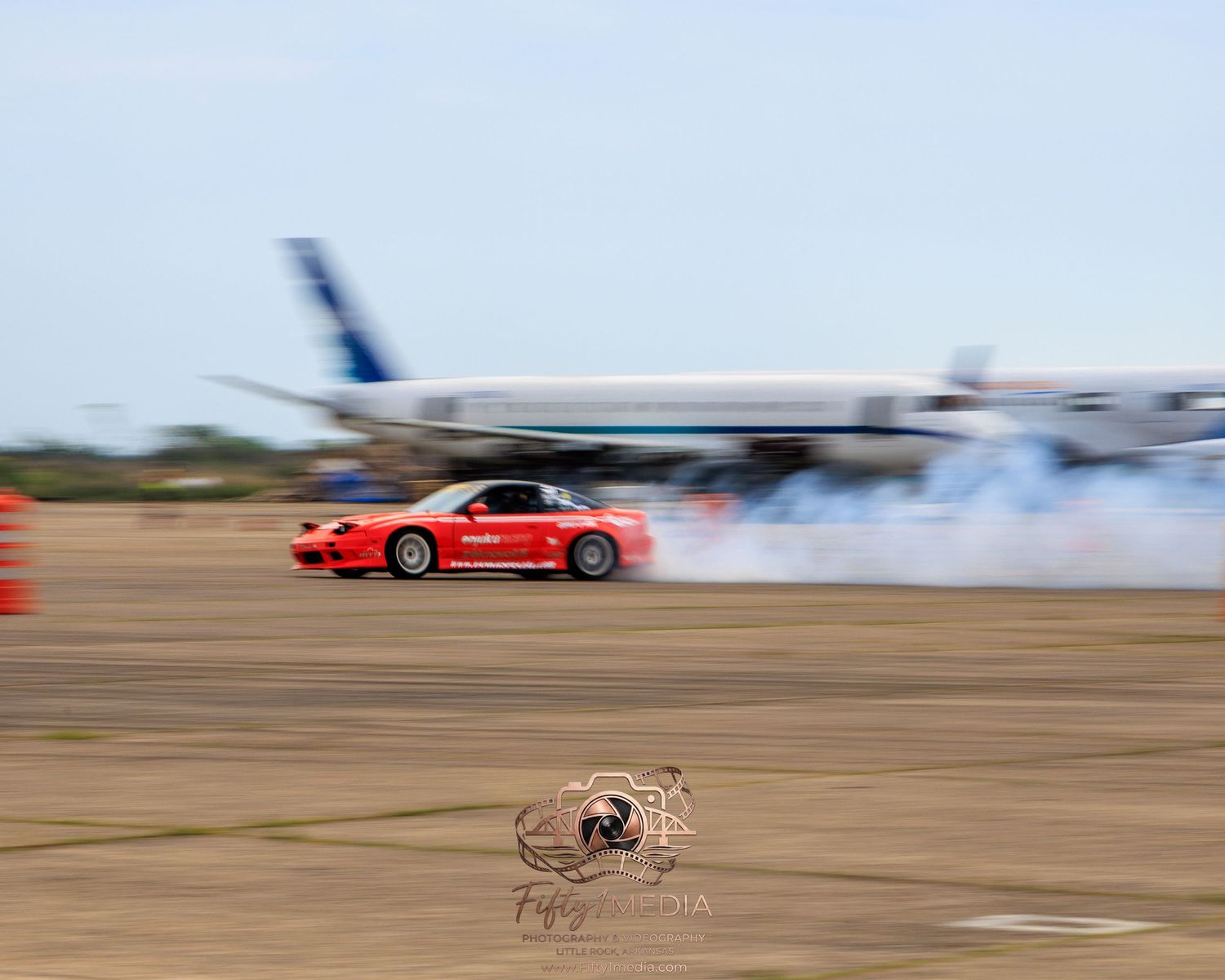 Red sports car drifting at high speed past a parked airplane in Arkansas by Fifty1Media.