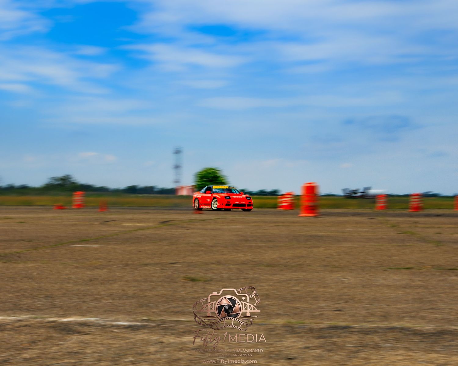 Orange traffic cones set up on a runway track for an automotive drift event under a blue sky.