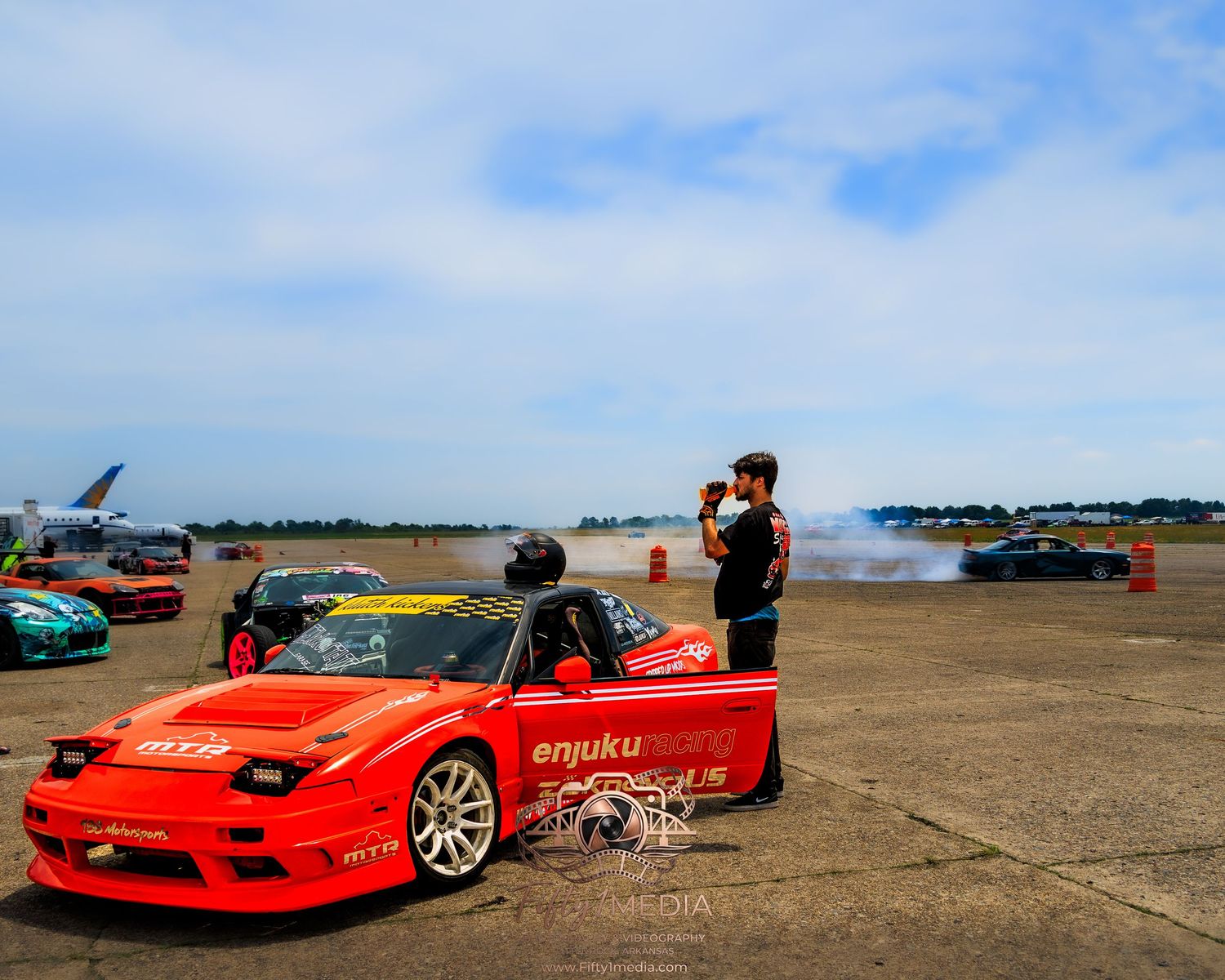 Car enthusiasts gathered around red sports cars at an outdoor track event in Central Arkansas.