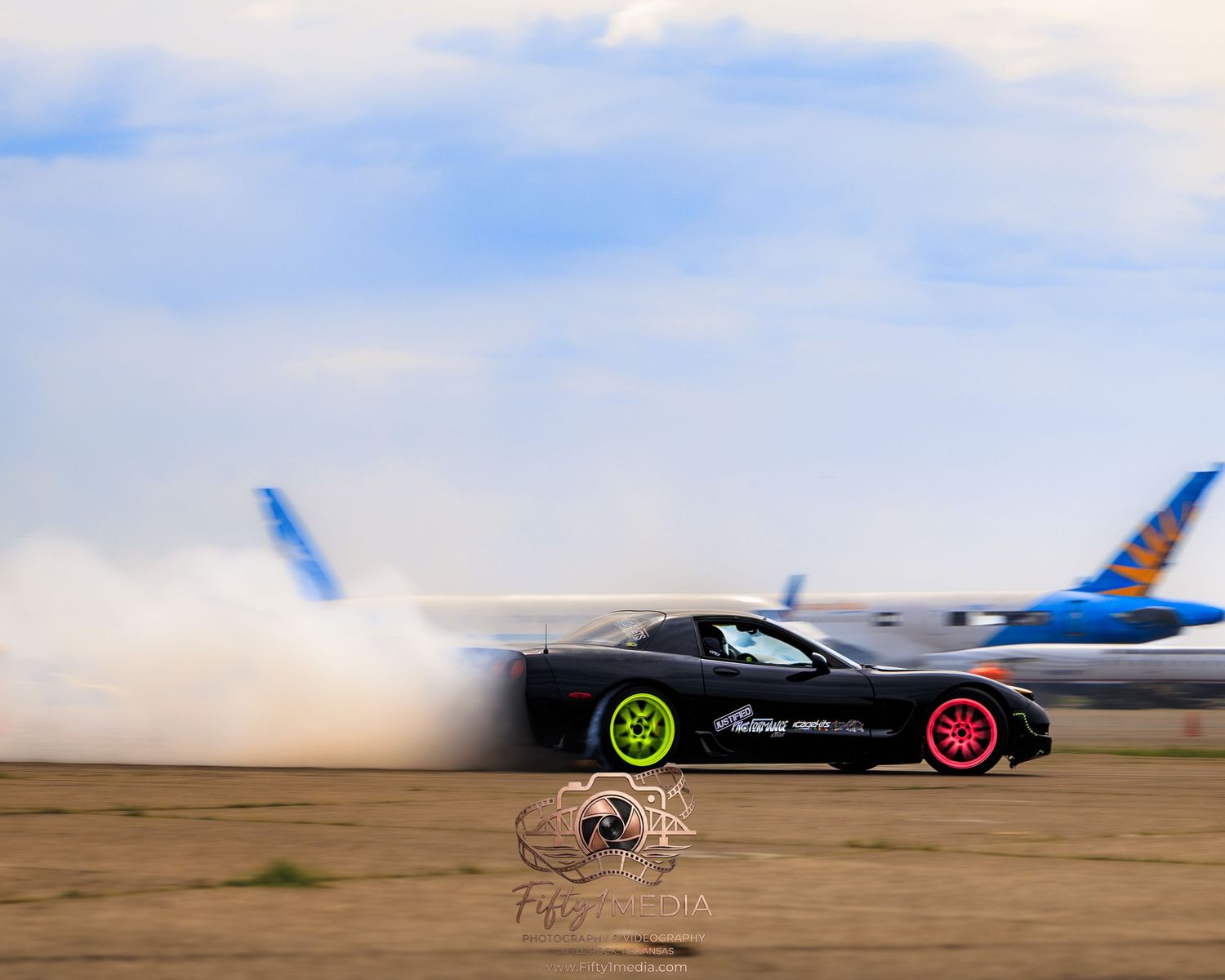 Dark drift car creating tire smoke while drifting past an airplane on a runway.