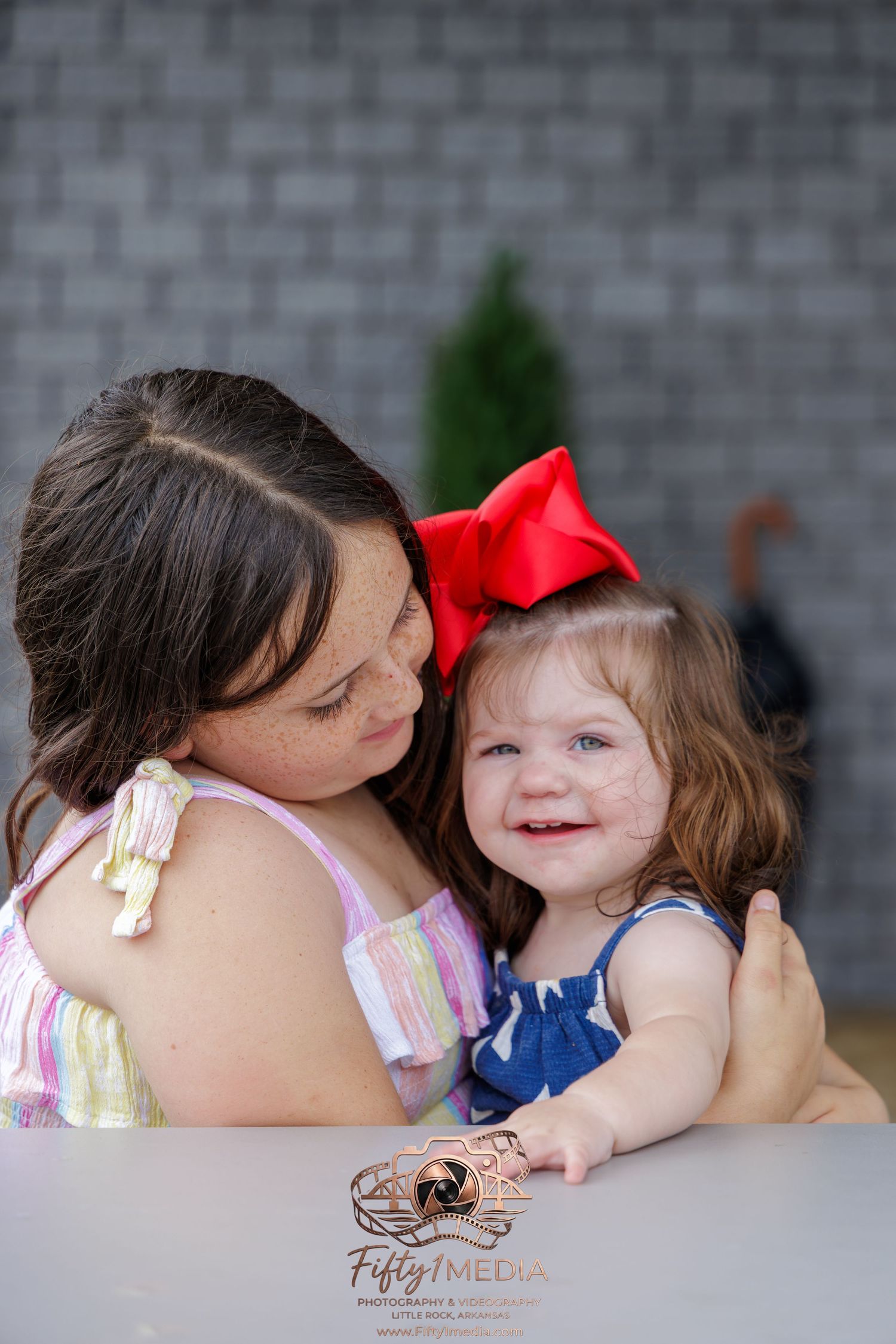 Studio portrait of a mother holding her smiling daughter who is wearing a red hair bow, Little Rock family photography.