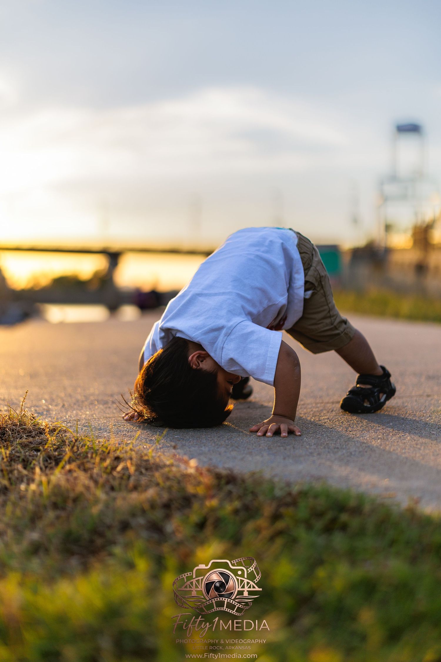 Young child playing on a sunny outdoor path near a bridge at sunset, Little Rock family photographer.
