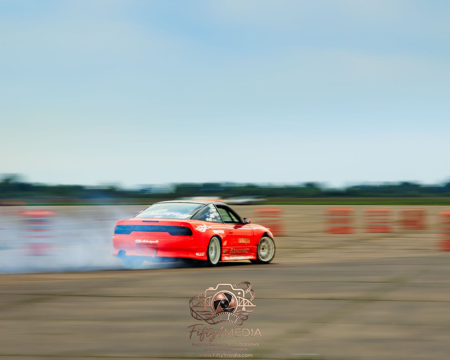 Red sports car drifting and creating tire smoke on an outdoor track.