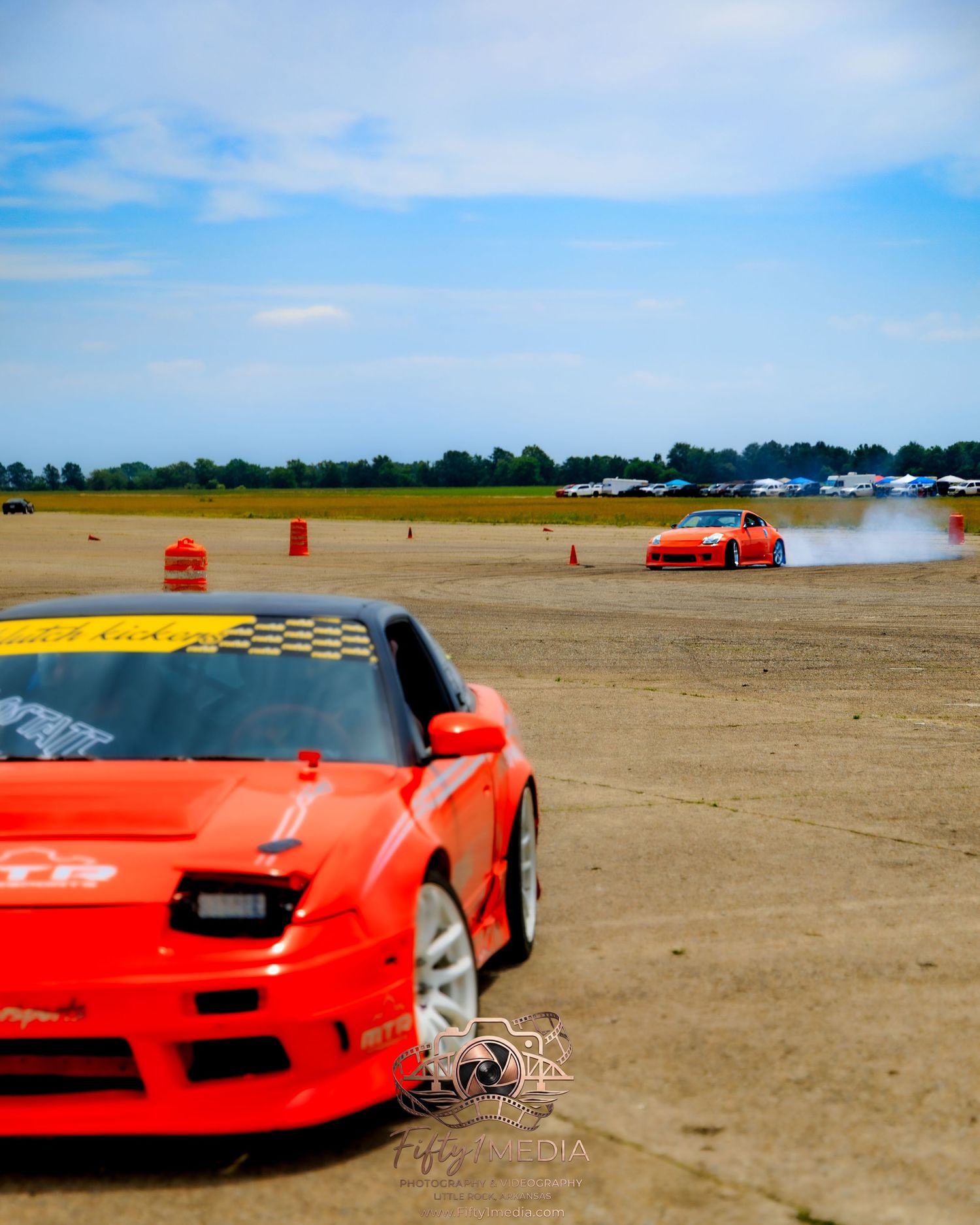 Front view of a red sports car parked on a runway track lined with orange cones.