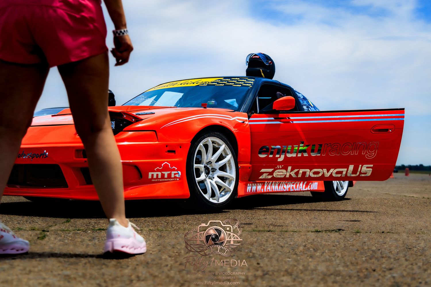 Driver sitting in a red sports car on an airport tarmac during an Arkansas automotive event.