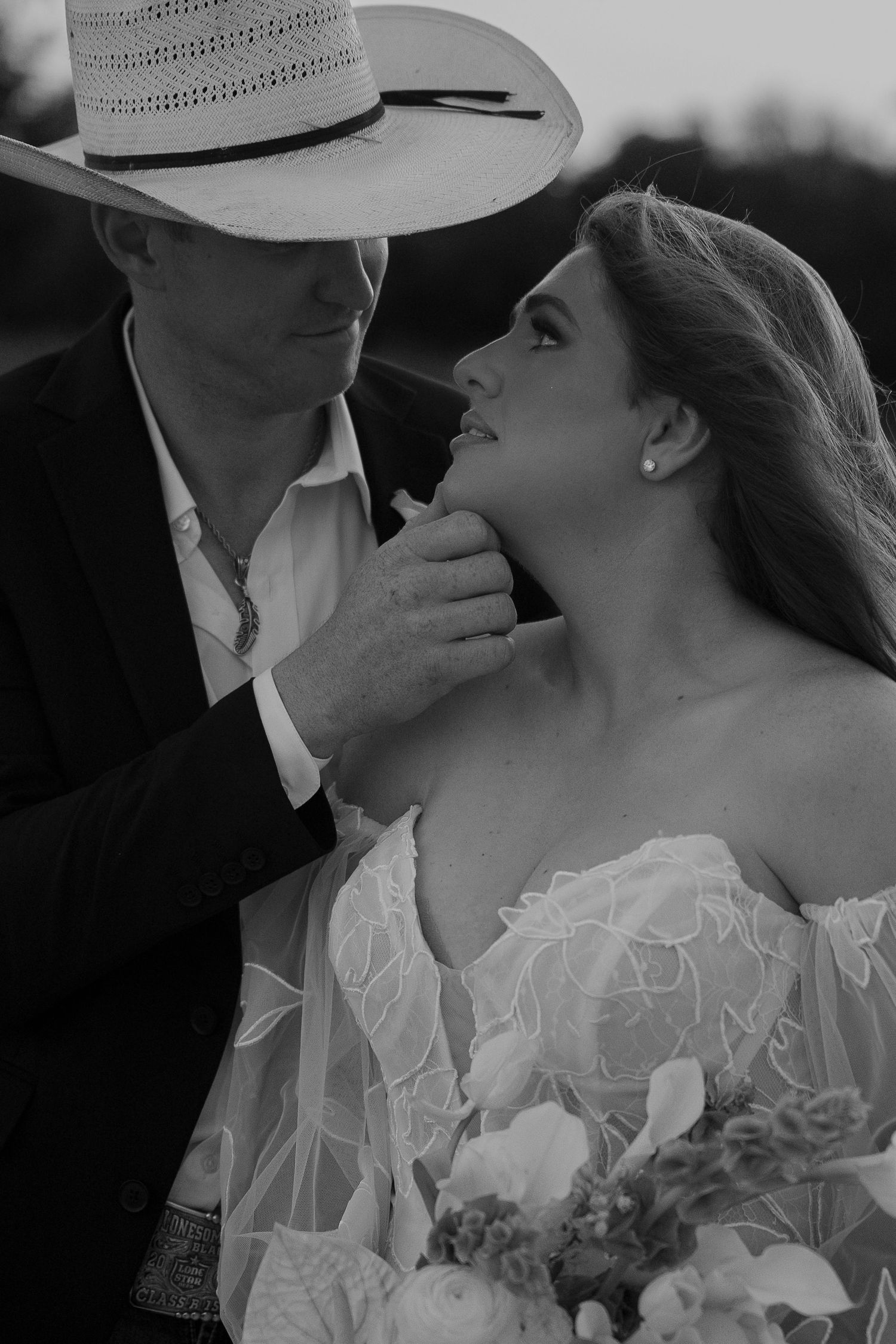 Groom in cowboy hat tenderly holds bride's face as she gazes up at him lovingly.