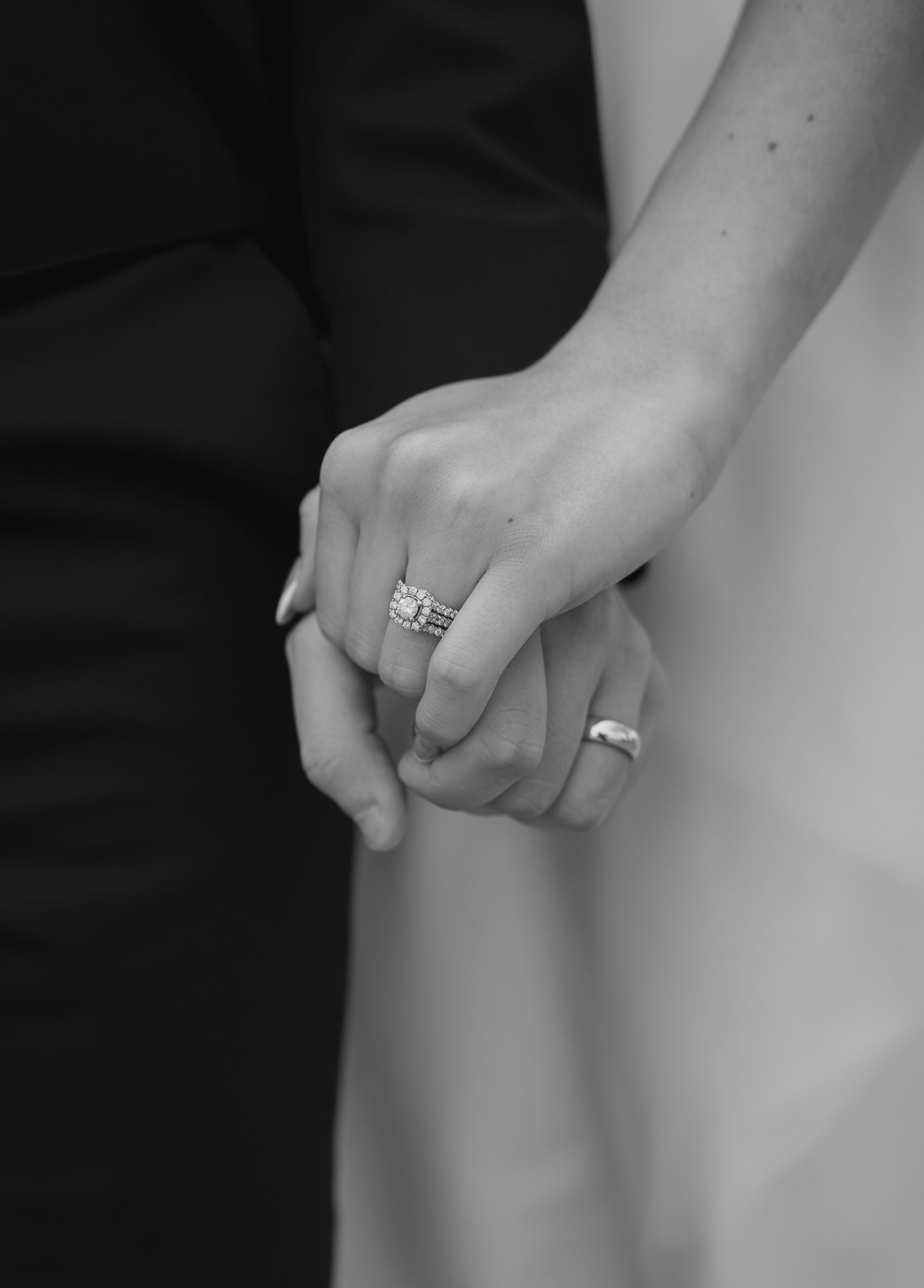 Black and white close-up of a bride and groom holding hands, showcasing a sparkling diamond engagement ring.