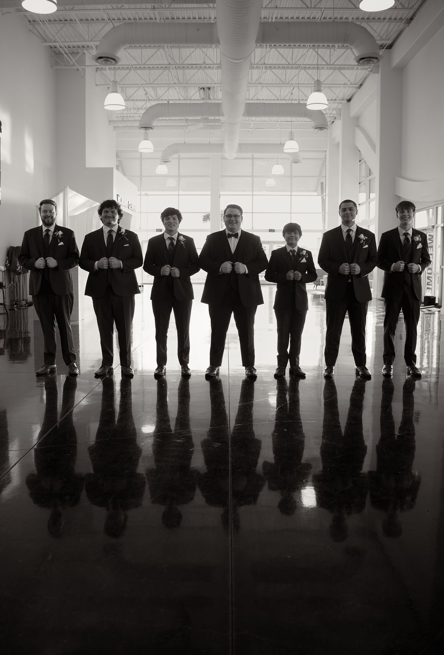 Black and white photo of groom and groomsmen in suits standing in a row on wedding day.
