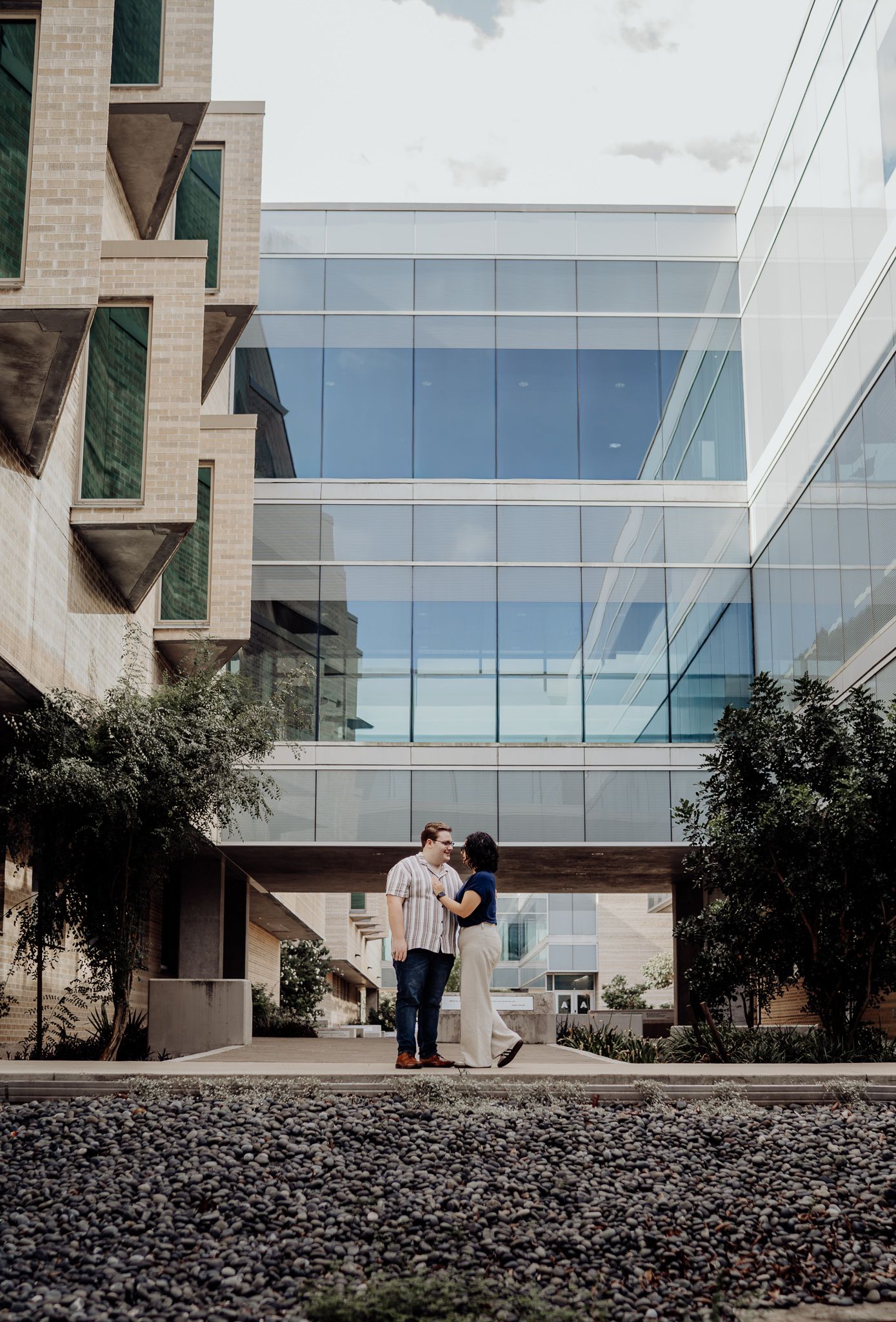 Couple standing together in front of a modern glass building during an engagement session.