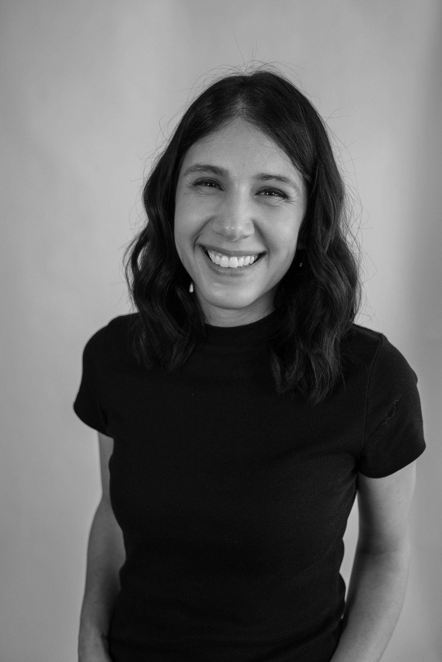 Black and white portrait of a smiling young woman with wavy hair in a black t-shirt.