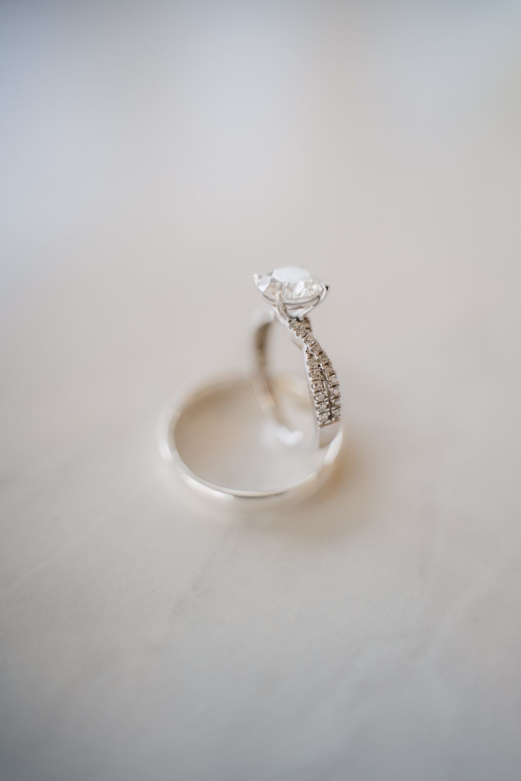 Elegant diamond solitaire engagement ring with pavé band displayed on white marble surface.