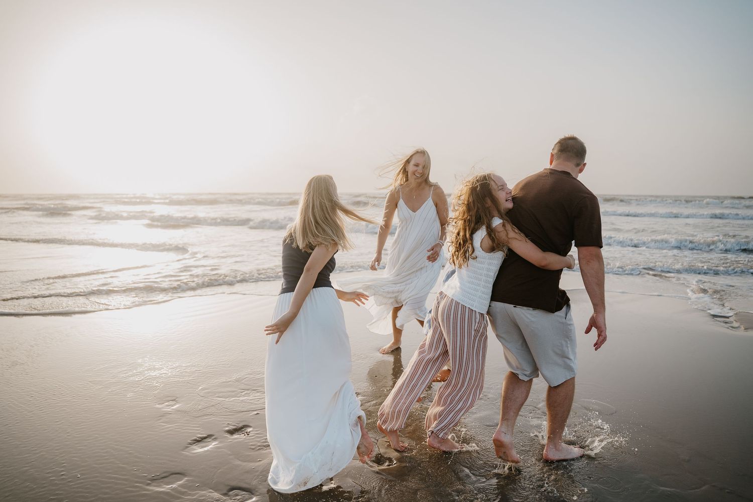 Family of four walking along a sunny beach shoreline, waves lapping at their feet during golden hour.