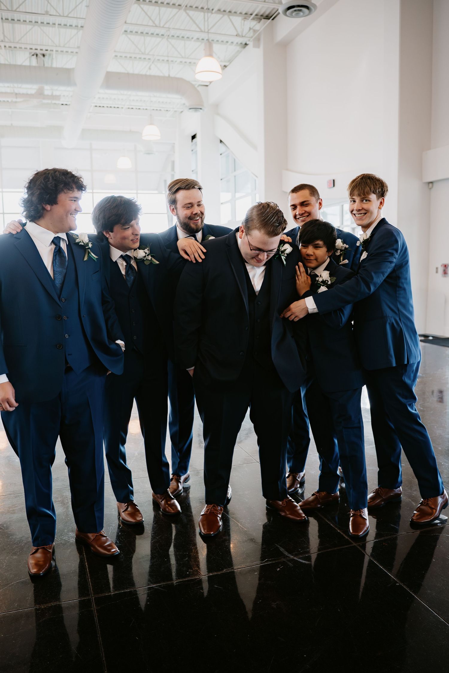 Groom and groomsmen laughing together in navy suits indoors.