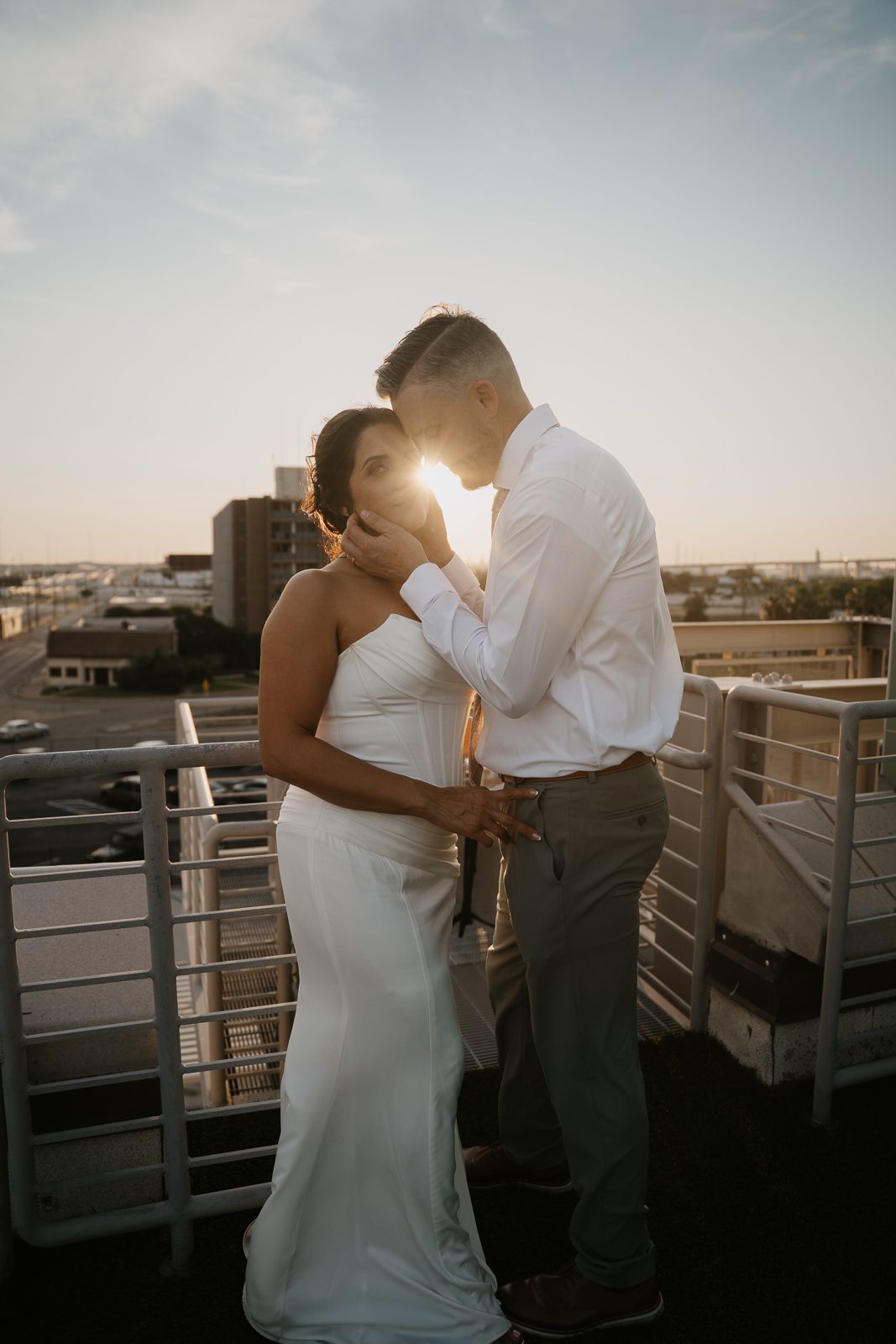 Bride and groom share a romantic sunset kiss on a rooftop with city views.