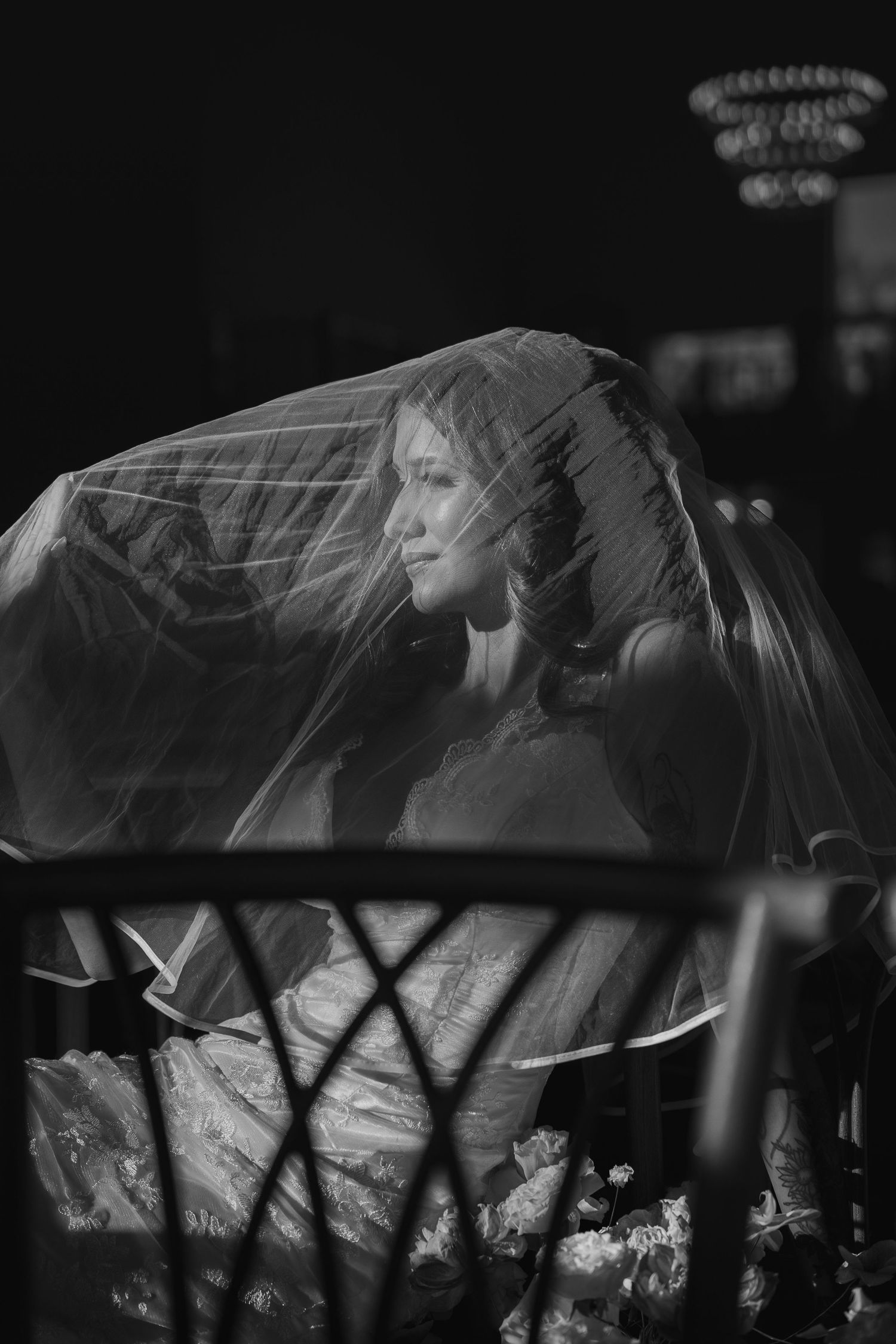 Black and white portrait of bride beneath veil in dramatic dark lighting.