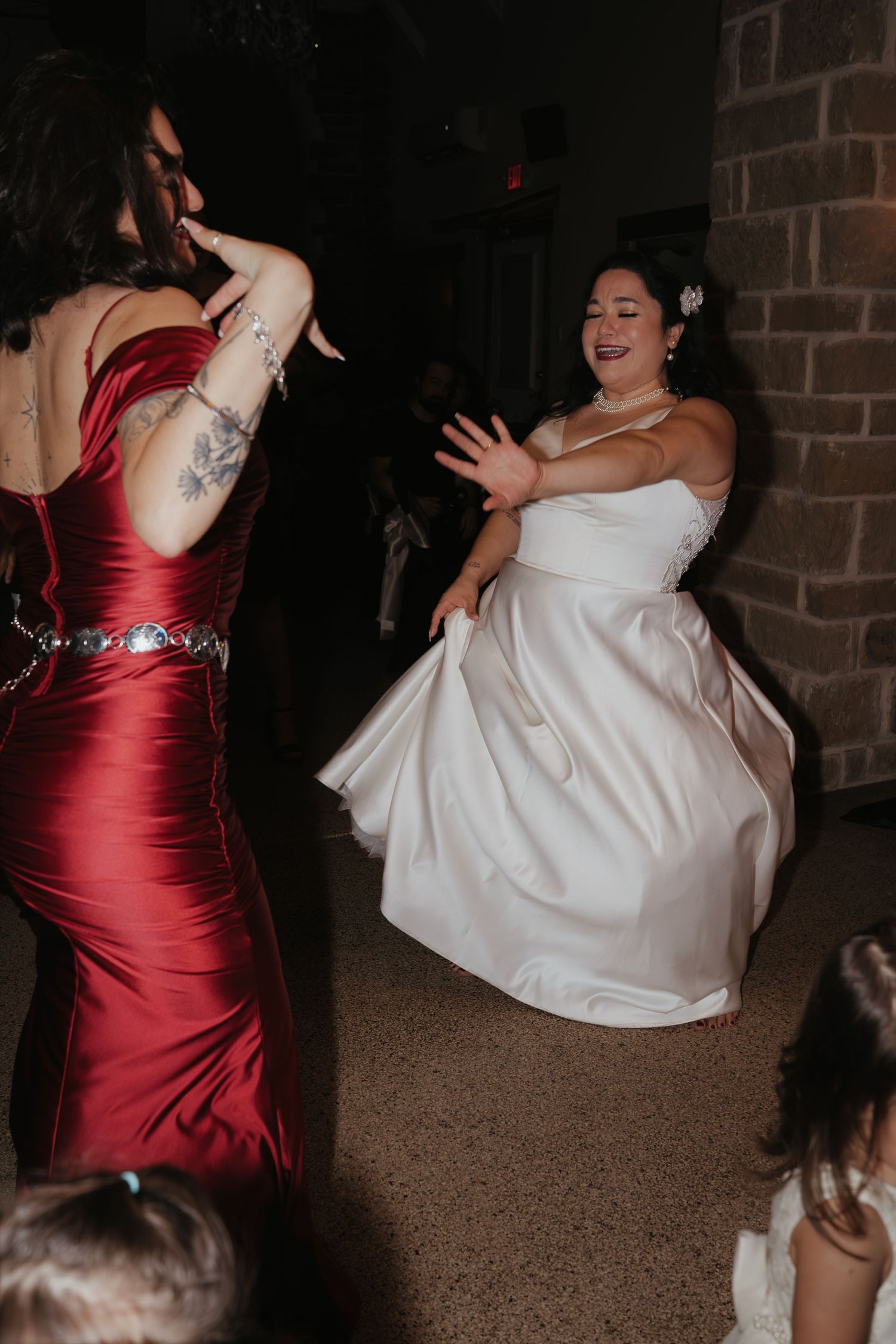 Bride in white gown dancing energetically with guest in red dress at wedding reception.