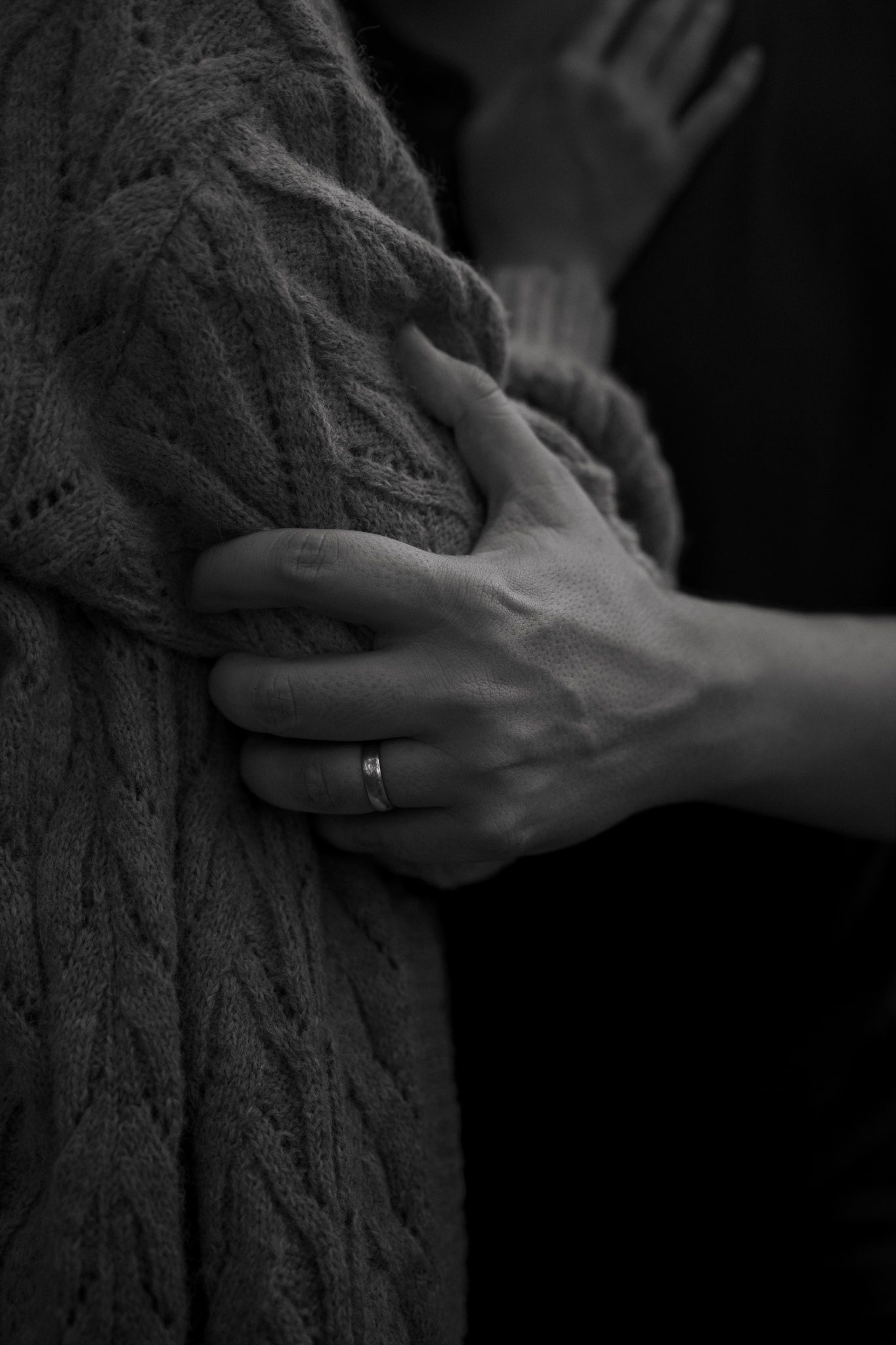Black and white close-up of couple embracing, hand with ring on cable knit sweater.