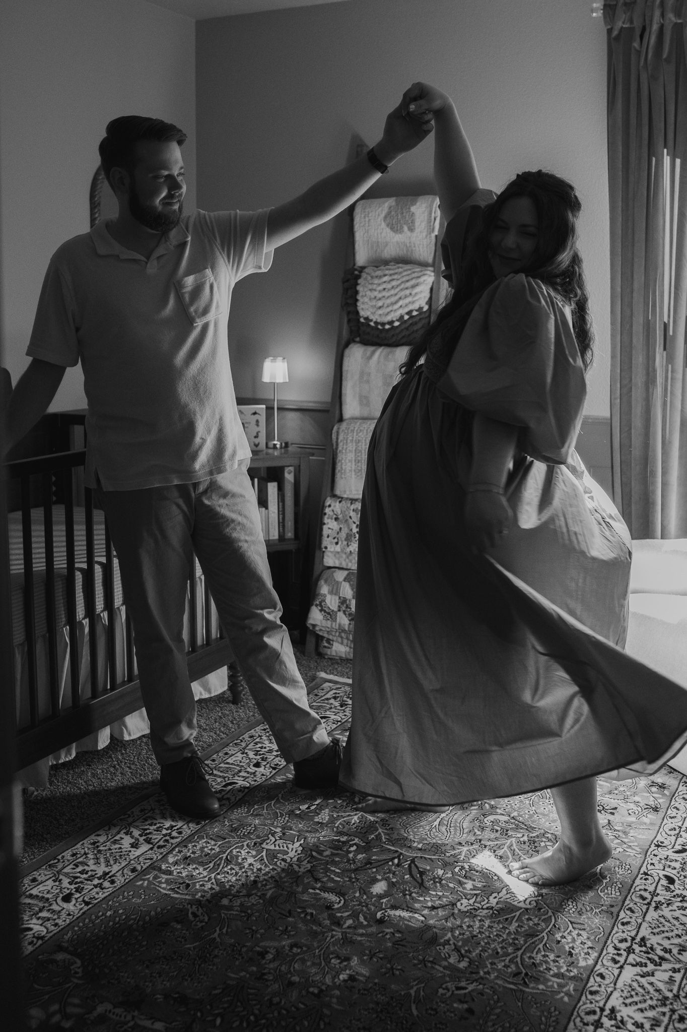 Couple dancing joyfully in nursery room in black and white maternity photography.