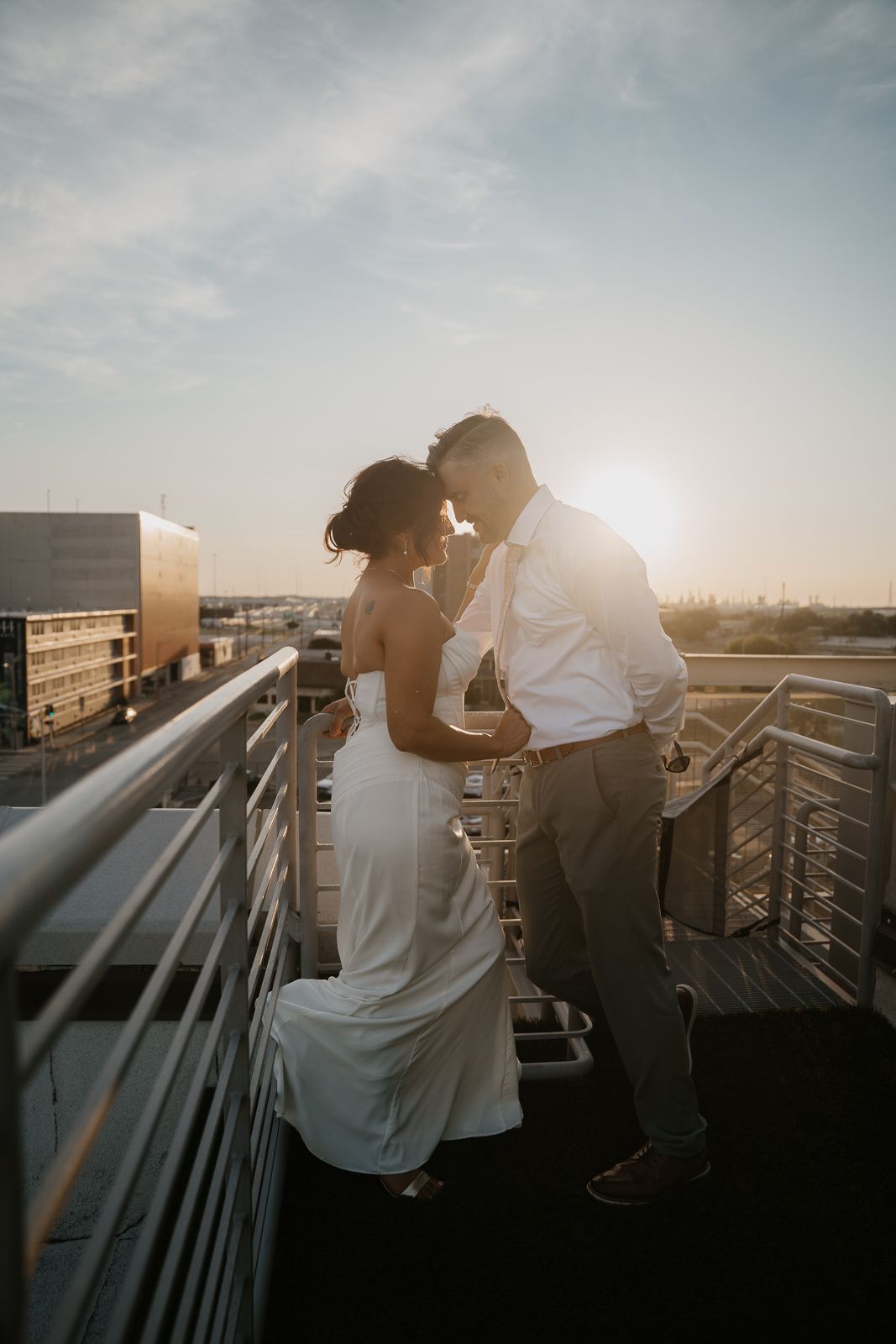 Bride and groom share a tender moment on a rooftop at golden hour with city skyline.