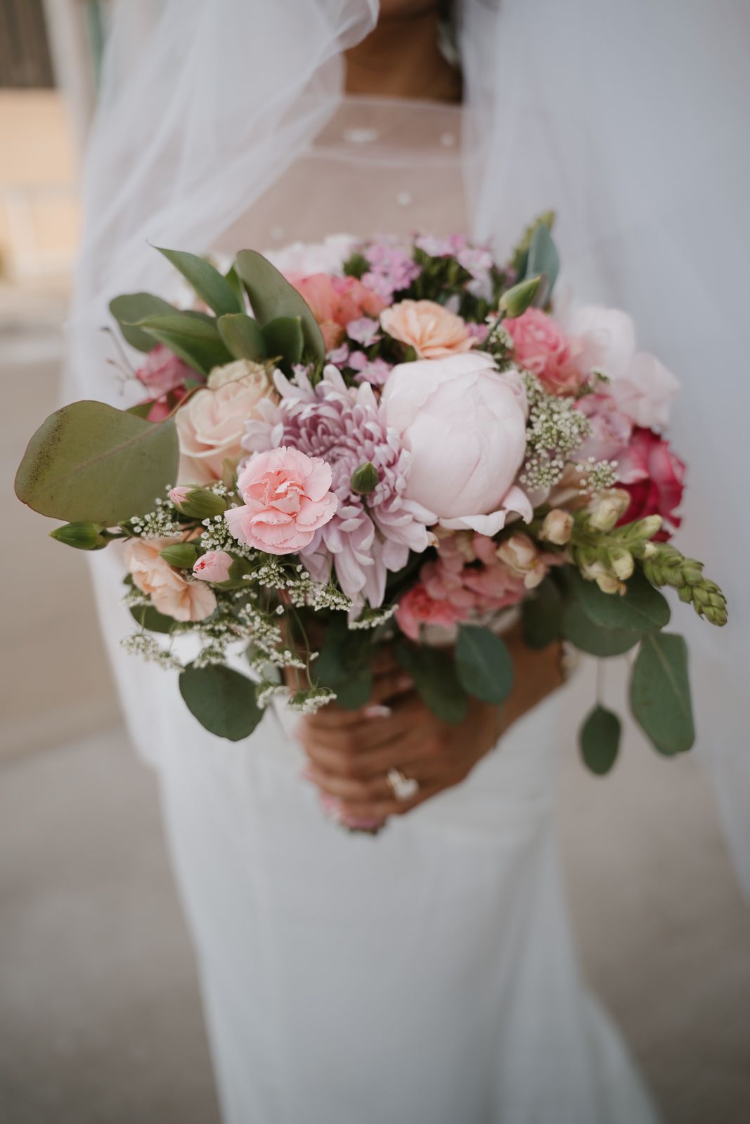 Bride holding a romantic pink and white wedding bouquet with roses and peonies.
