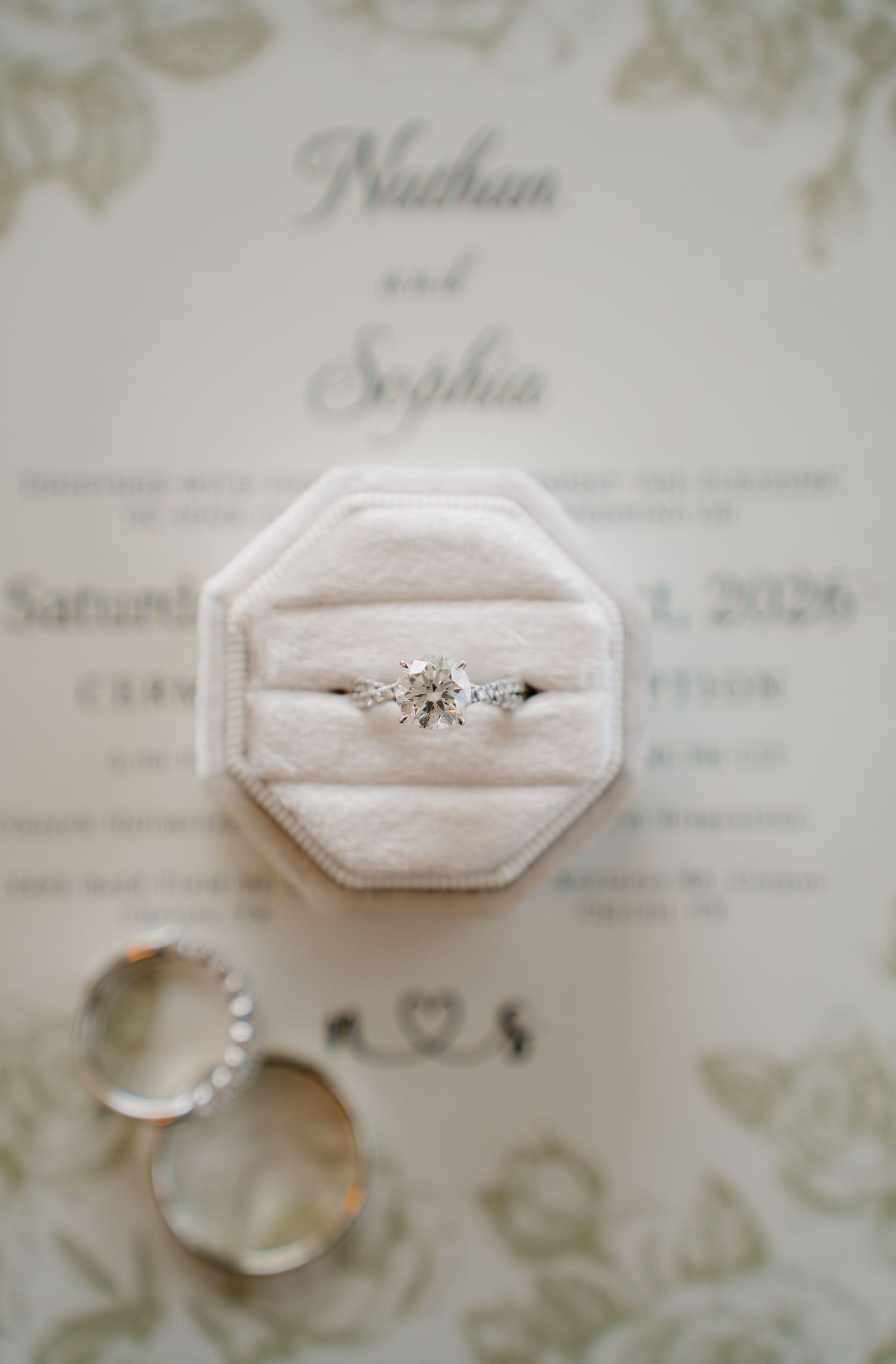 Wedding rings and diamond engagement ring displayed on floral invitation for Nathan and Sophia.