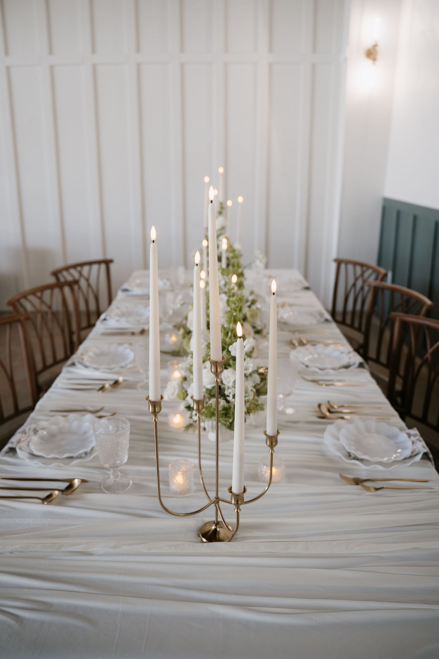 Elegant wedding reception table with gold candelabra, white taper candles, and floral centerpiece.