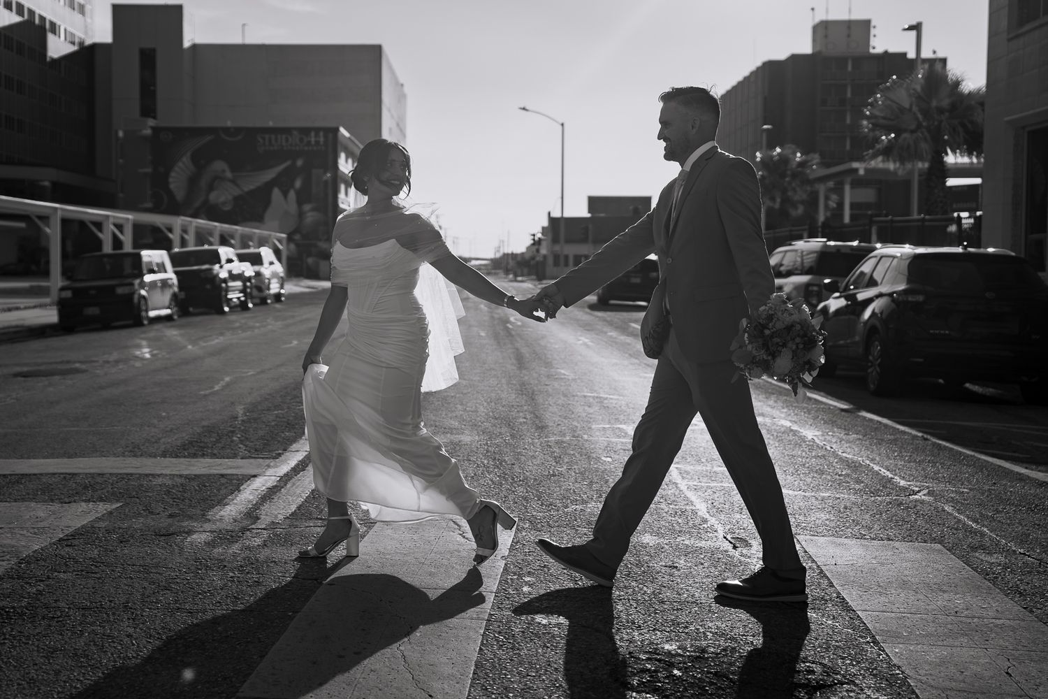 Bride and groom holding hands crossing city street in black and white wedding photo.