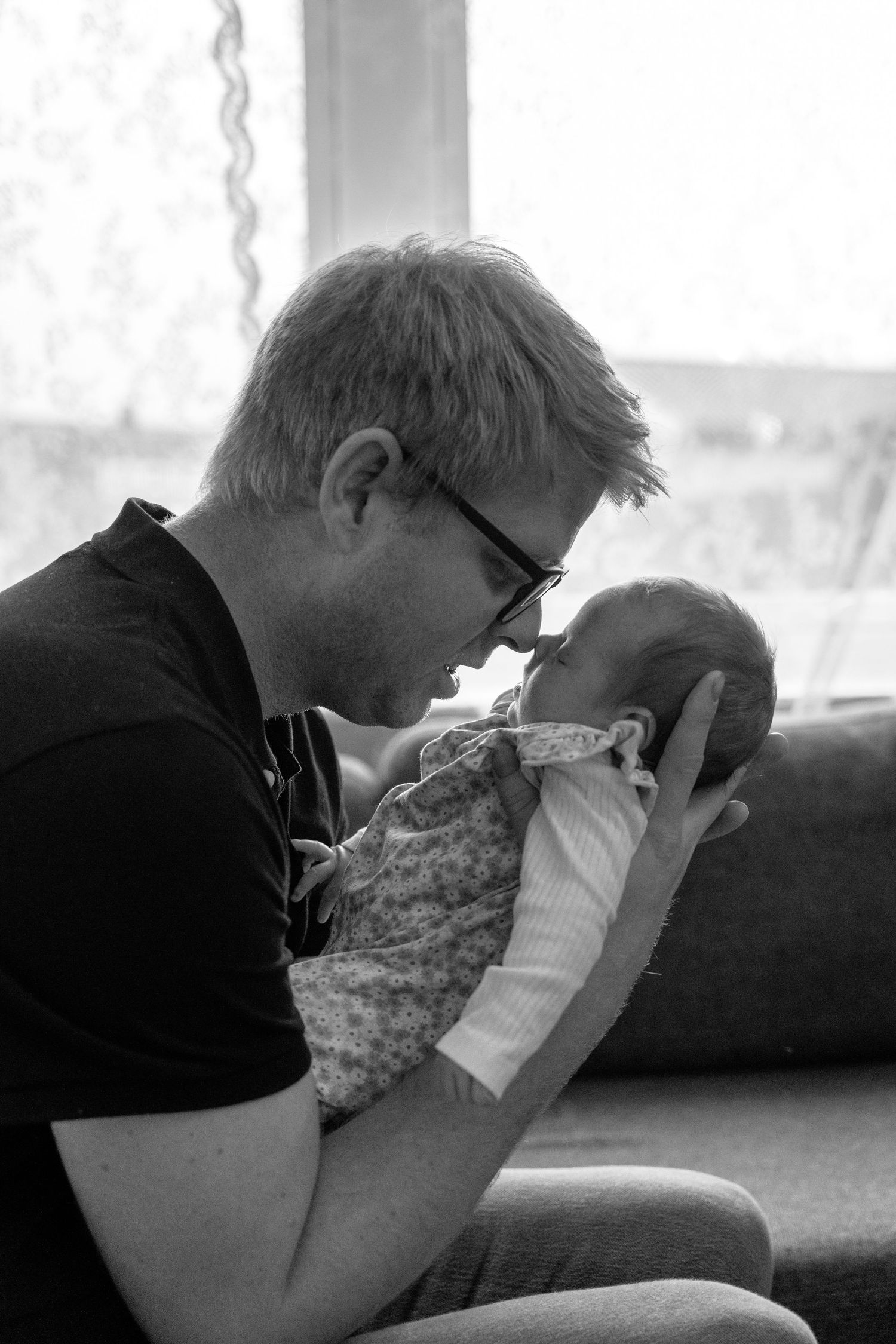 Tender black and white photo of a dad pressing his forehead against his newborn baby.