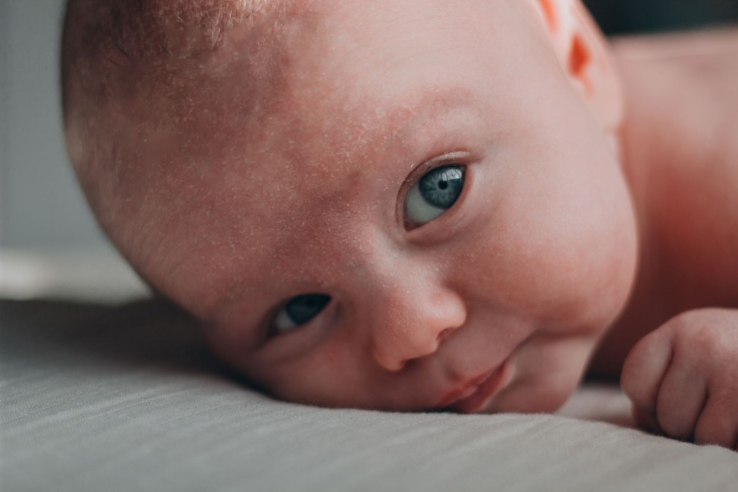 Close-up portrait of a newborn baby with blue eyes lying on their tummy on a soft surface.