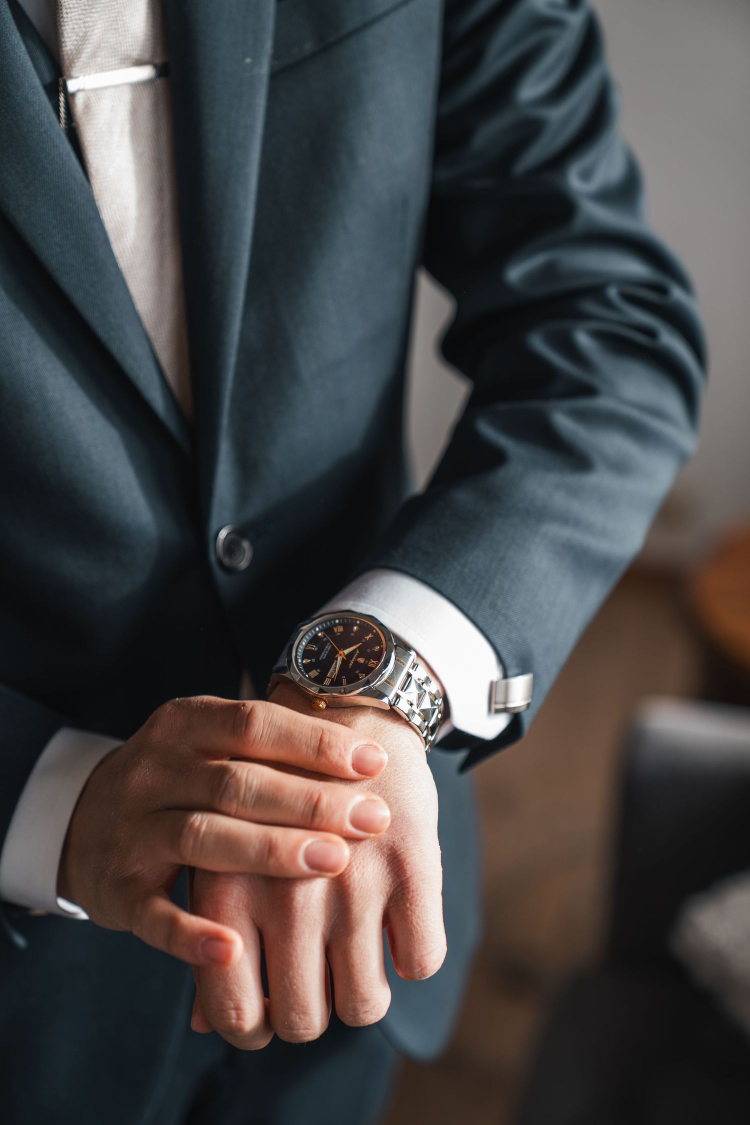 Close-up of groom in navy suit adjusting his silver wristwatch on wedding day.