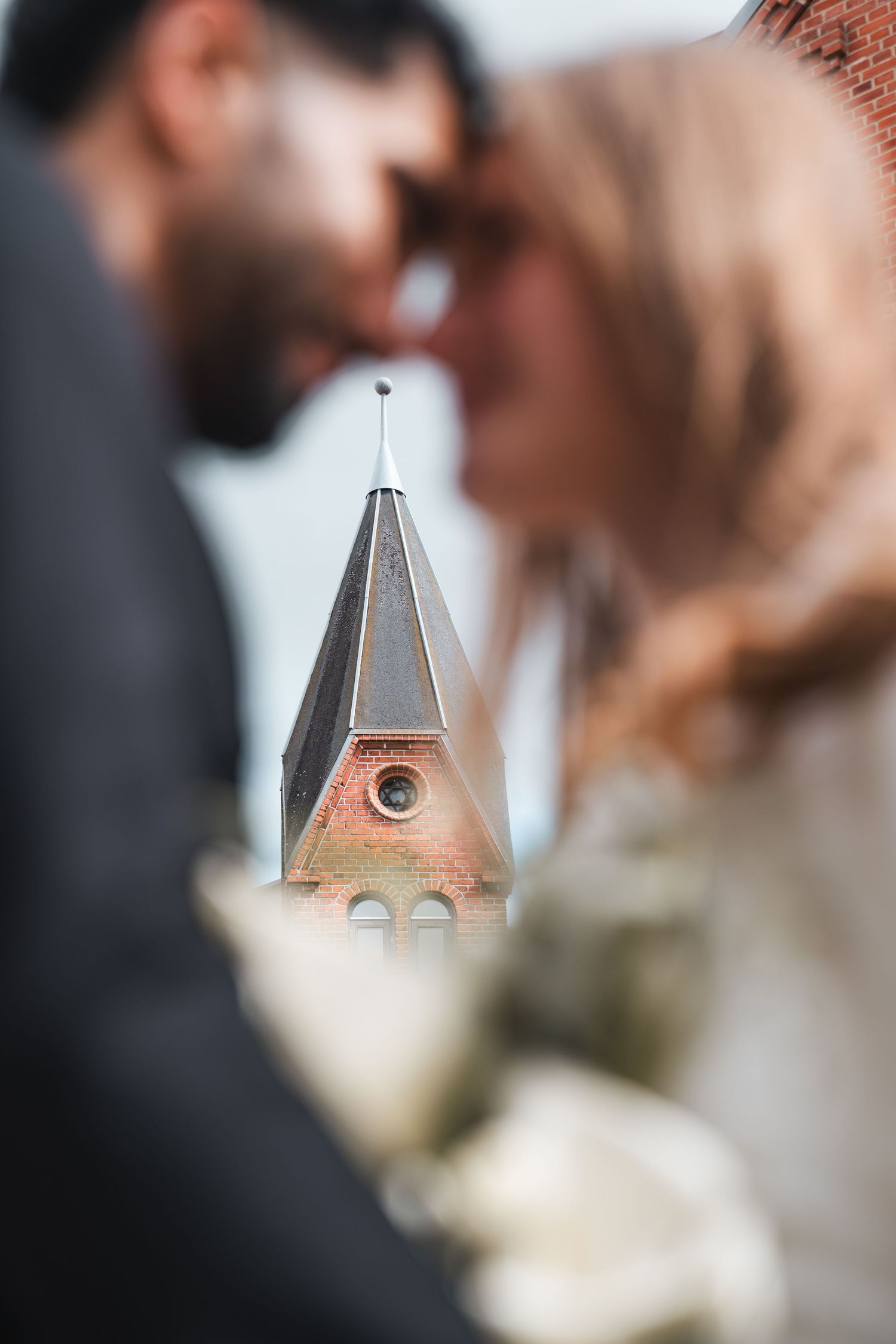 Bride and groom sharing romantic moment with blurred church steeple in background.