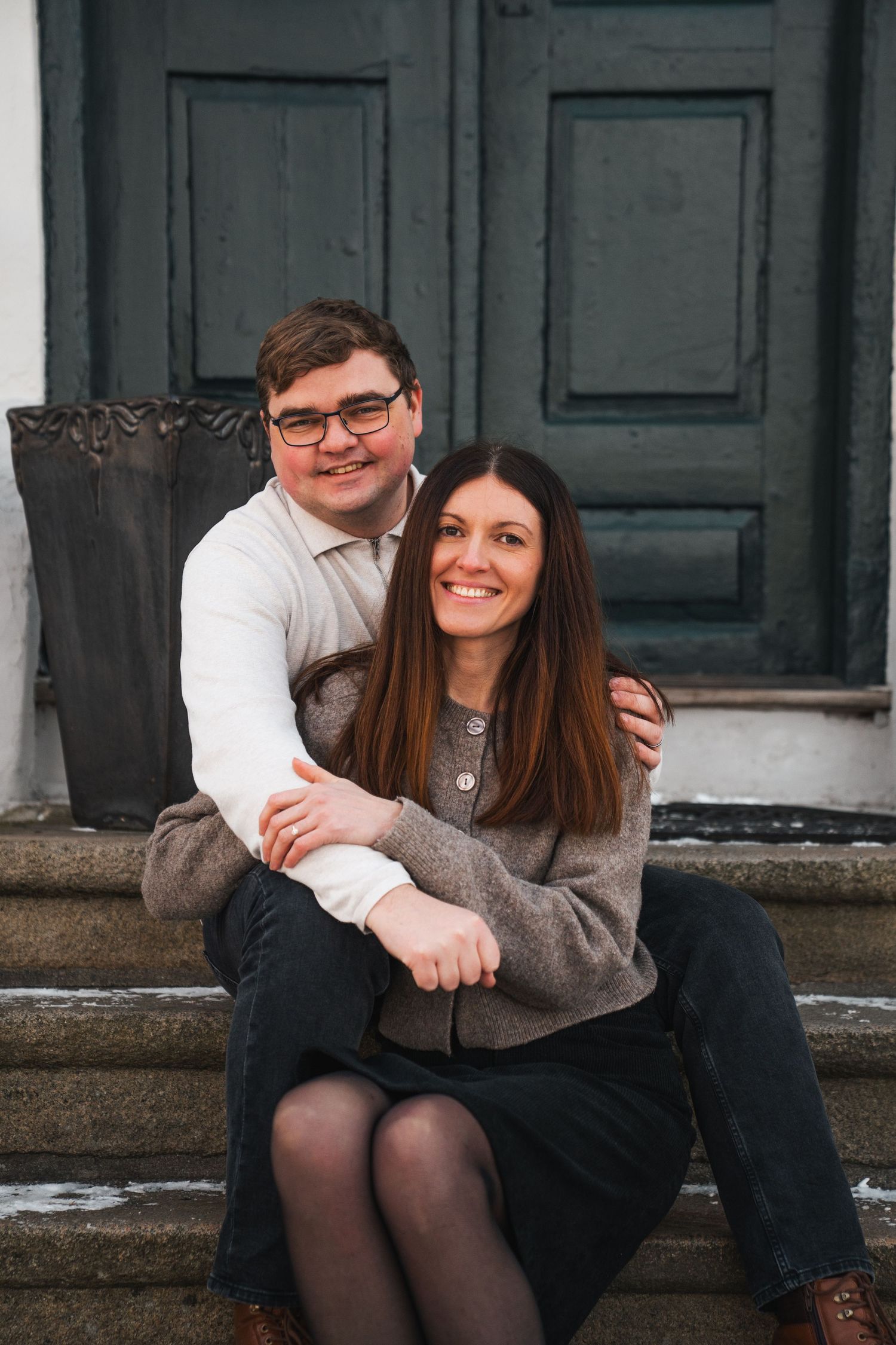 Smiling couple sitting on steps in front of green door embracing warmly.