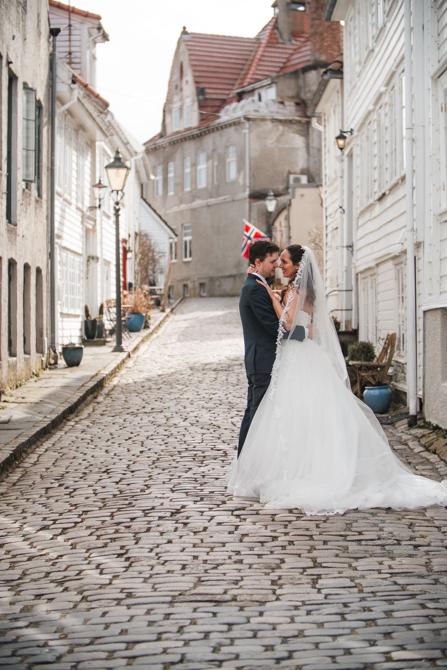 Bride and groom kissing on cobblestone street in charming European old town.