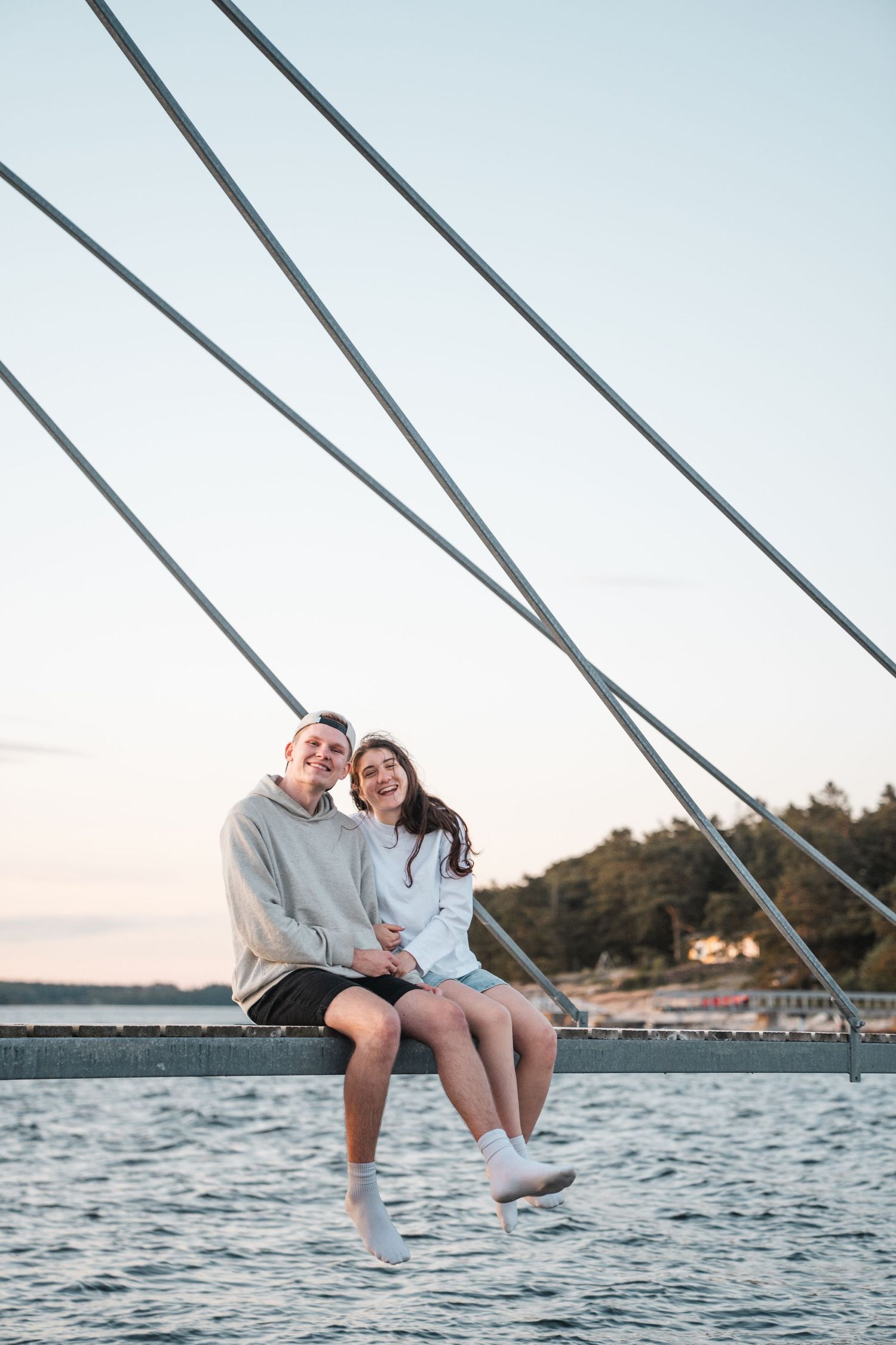 Happy couple sitting together on bridge railing over water at dusk.