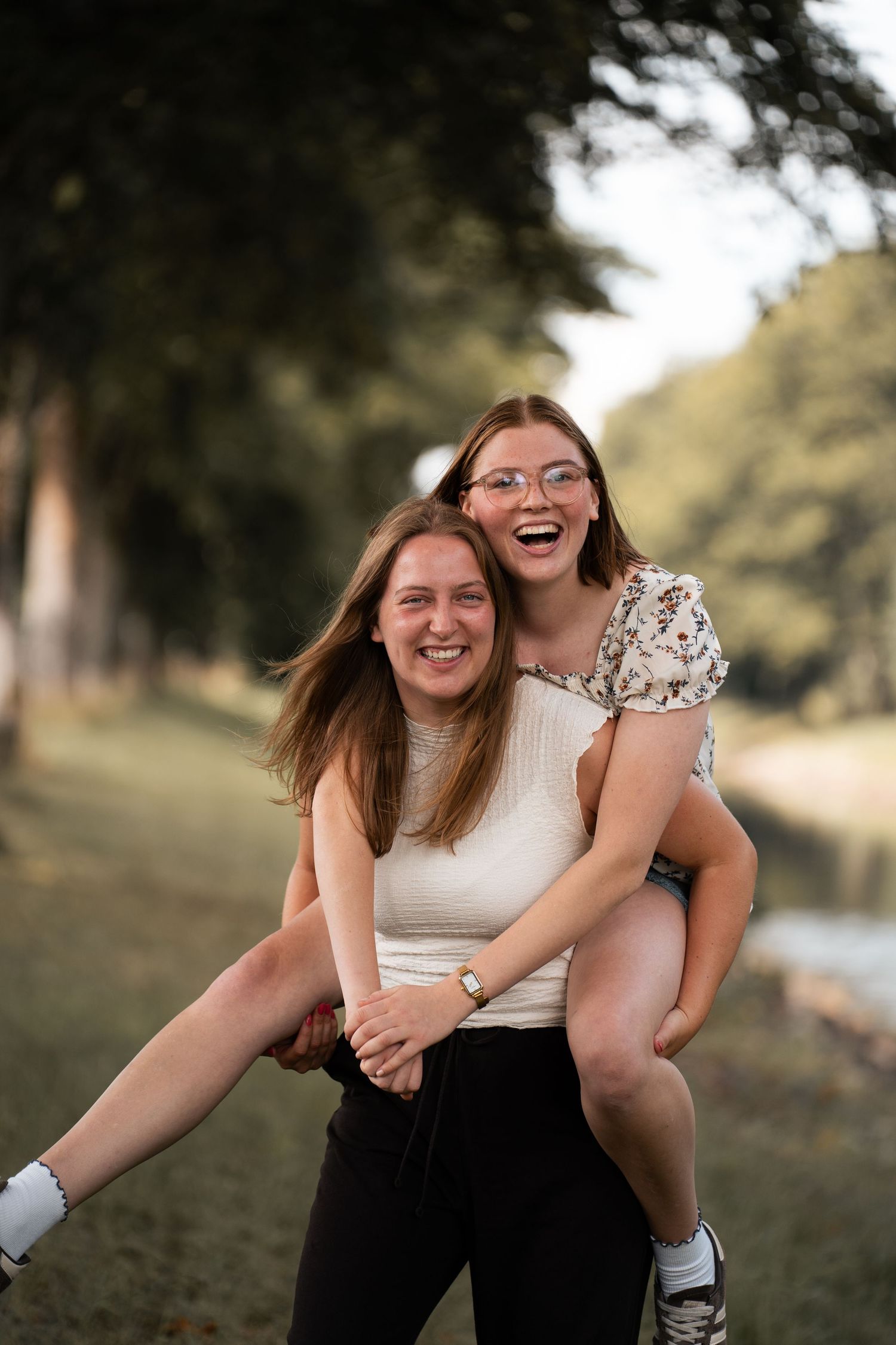 Two joyful young women giving piggyback ride while laughing in a green park.
