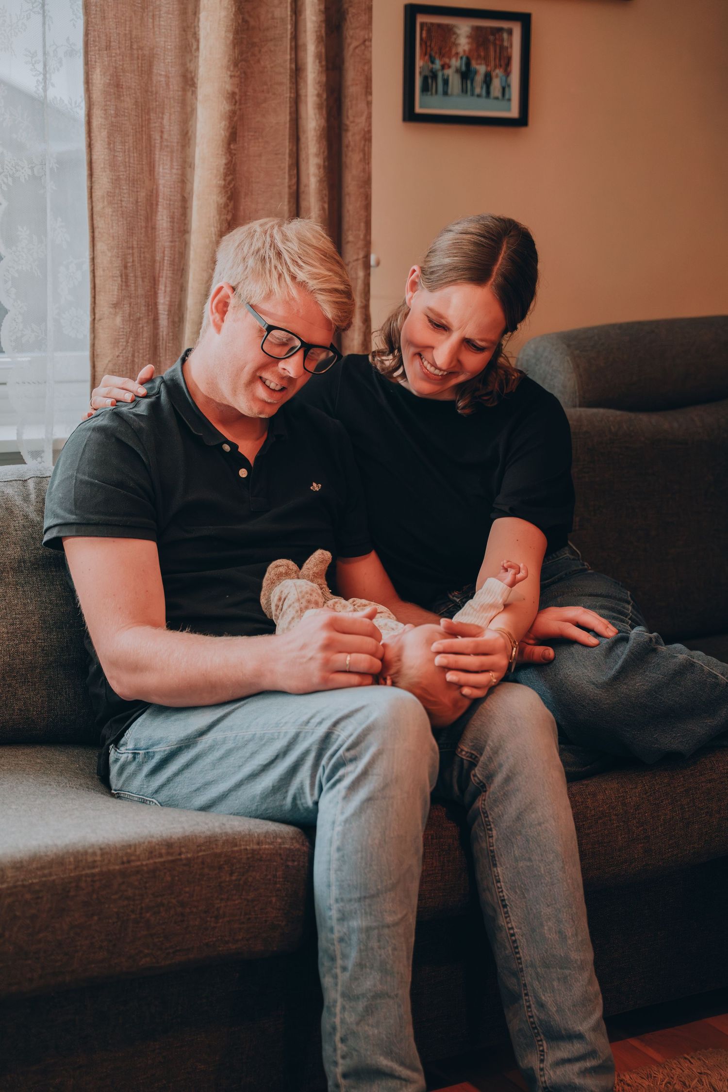 Happy couple sitting on a sofa together holding their newborn baby's tiny feet.