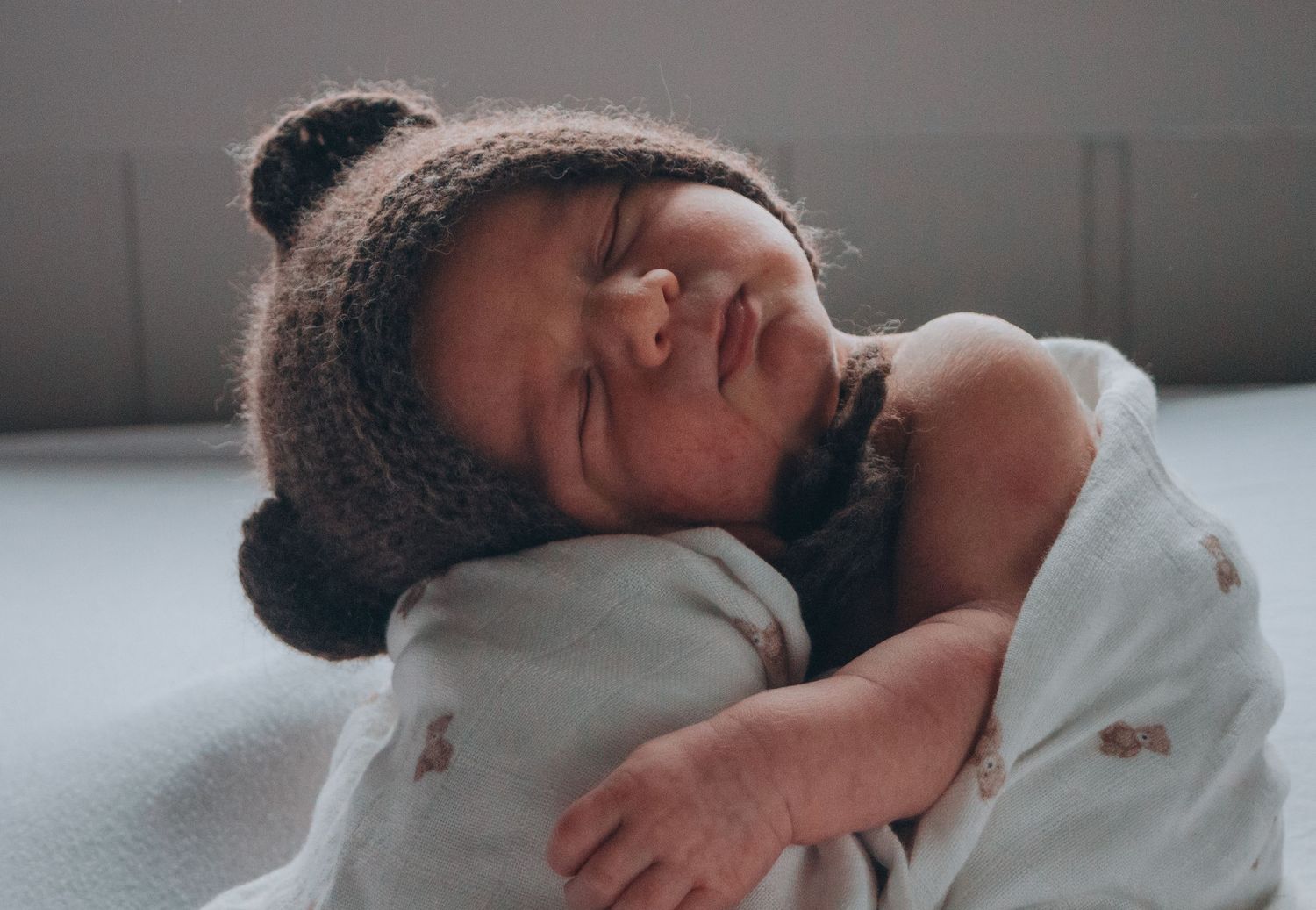 Sleeping newborn baby wearing a cute brown bear ear knit hat wrapped in a soft blanket.