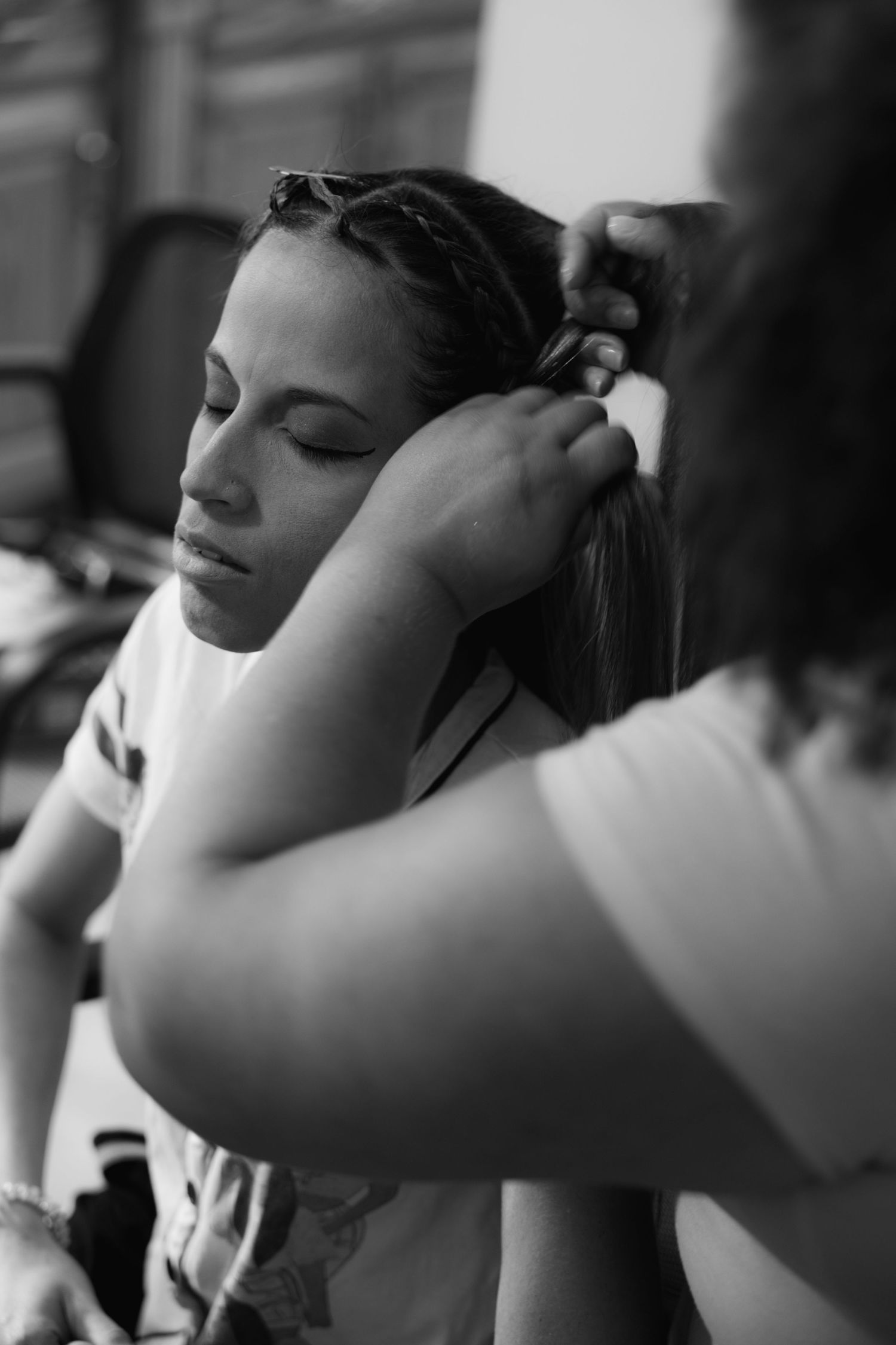 Black and white photo of woman having her hair styled by a hairdresser before a wedding ceremony.