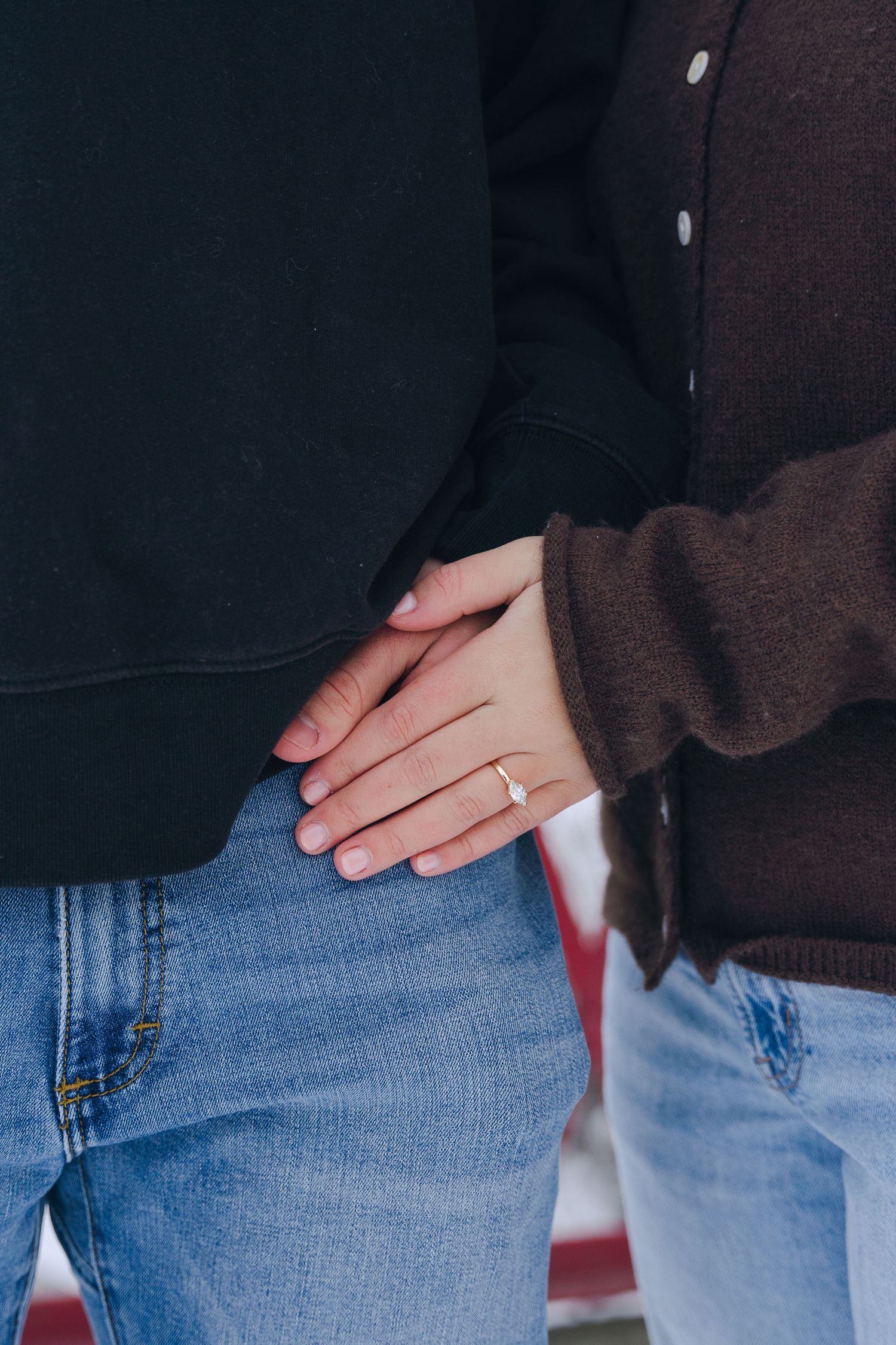 Close-up of a woman's hand with an engagement ring resting on a man's jeans, both wearing casual outfits.
