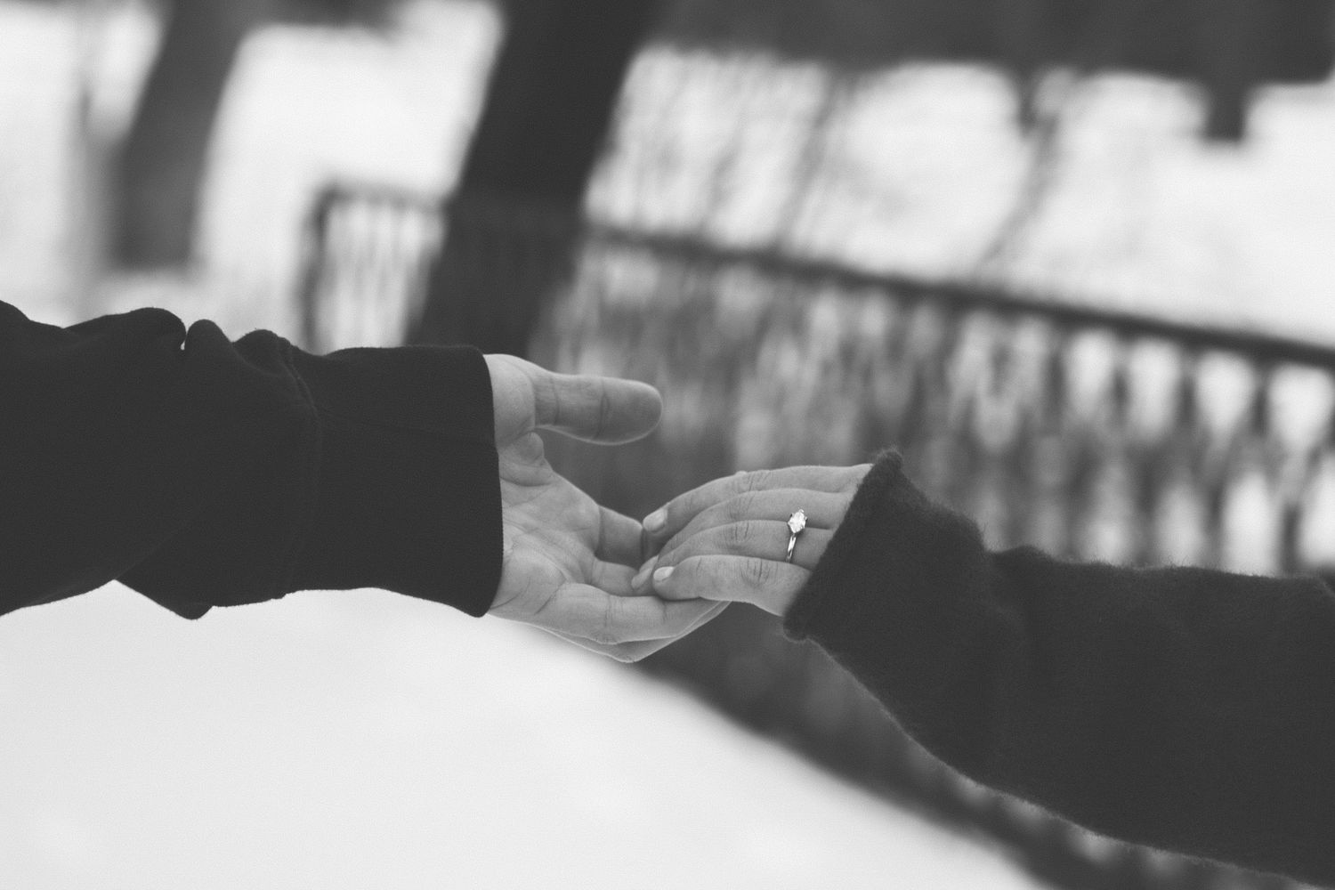 Black and white photo of two hands exchanging a ring, symbolizing a romantic proposal or engagement.