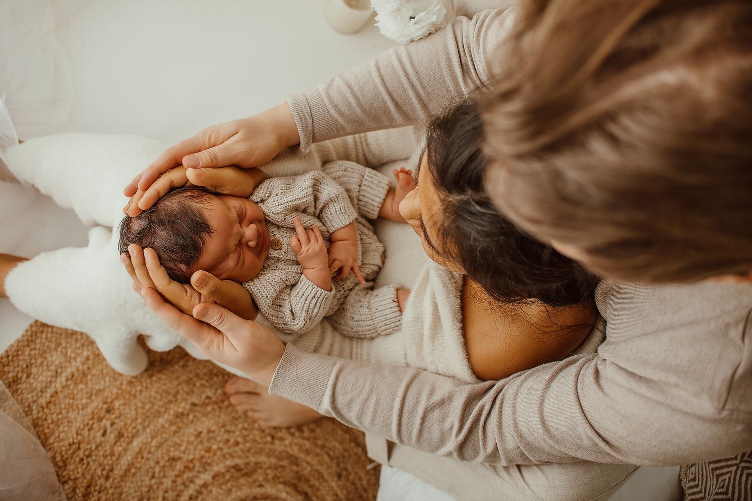 A mother tenderly gazes at her newborn baby cradled in gentle hands on a soft white surface.