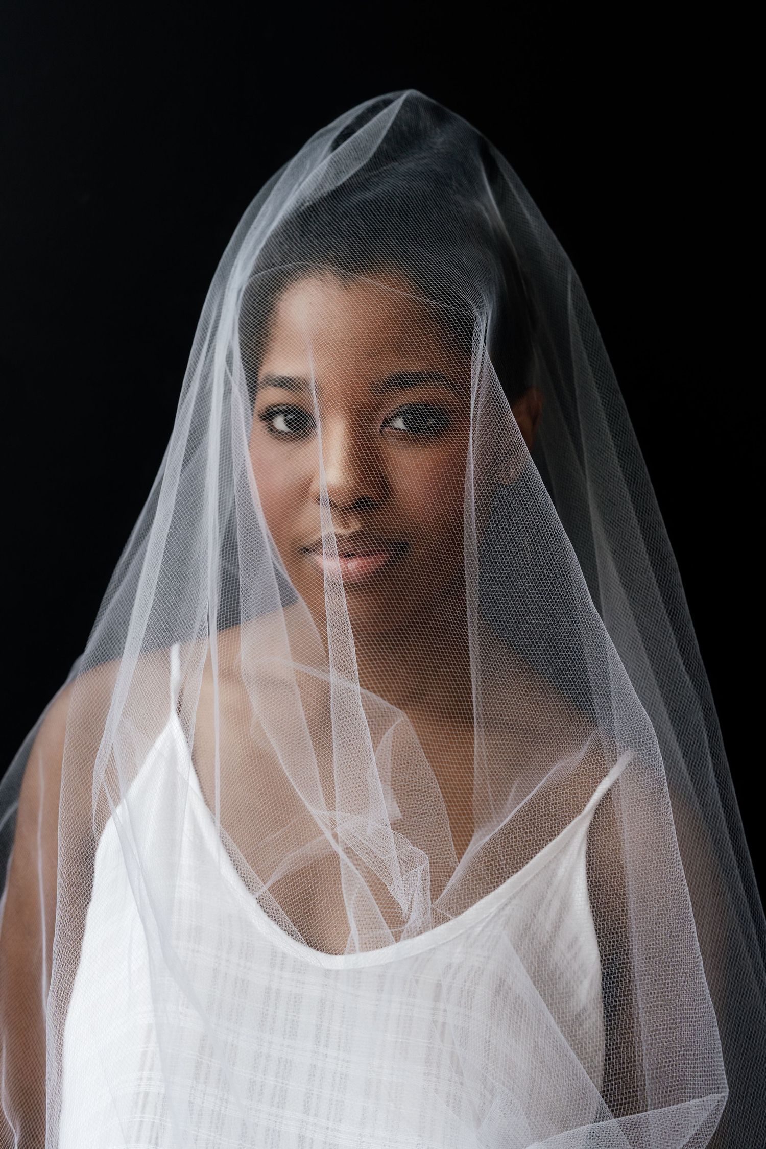 A bride wearing a white wedding dress and veil poses against a dark background in a series of elegant portraits.