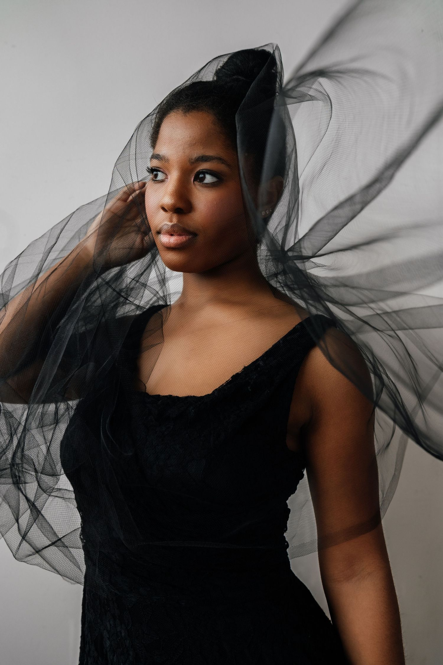 Artistic fashion portrait series showing flowing black tulle fabric against white background creating dramatic movement.