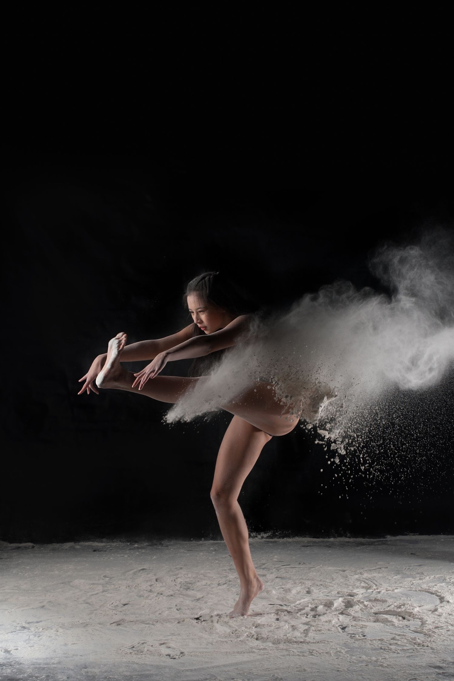Dramatic dance performance with white powder creating ethereal effects against dark background as dancer moves in leotard.